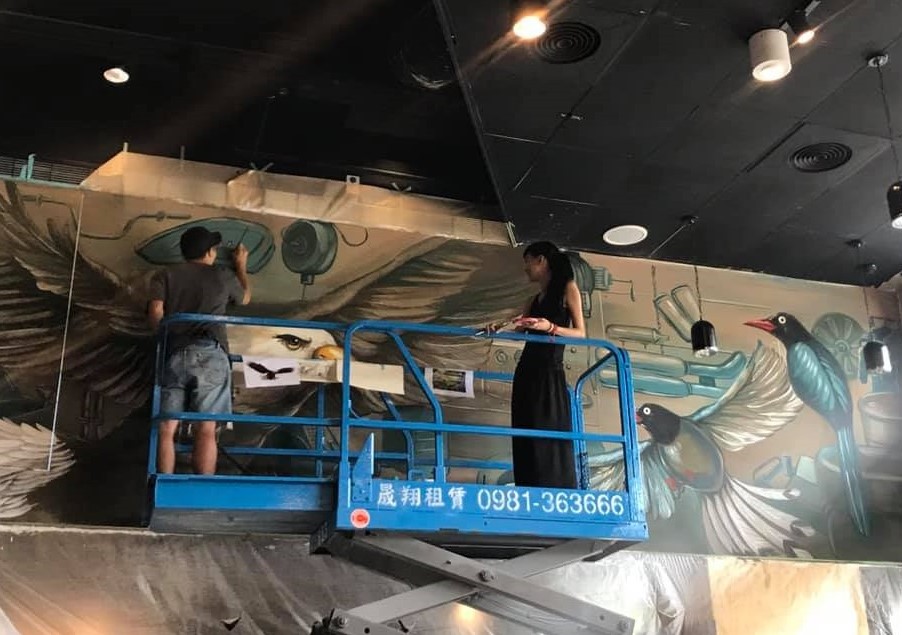 她帶一名助手上堆高自走車，幫印地安美式重機畫壁畫。