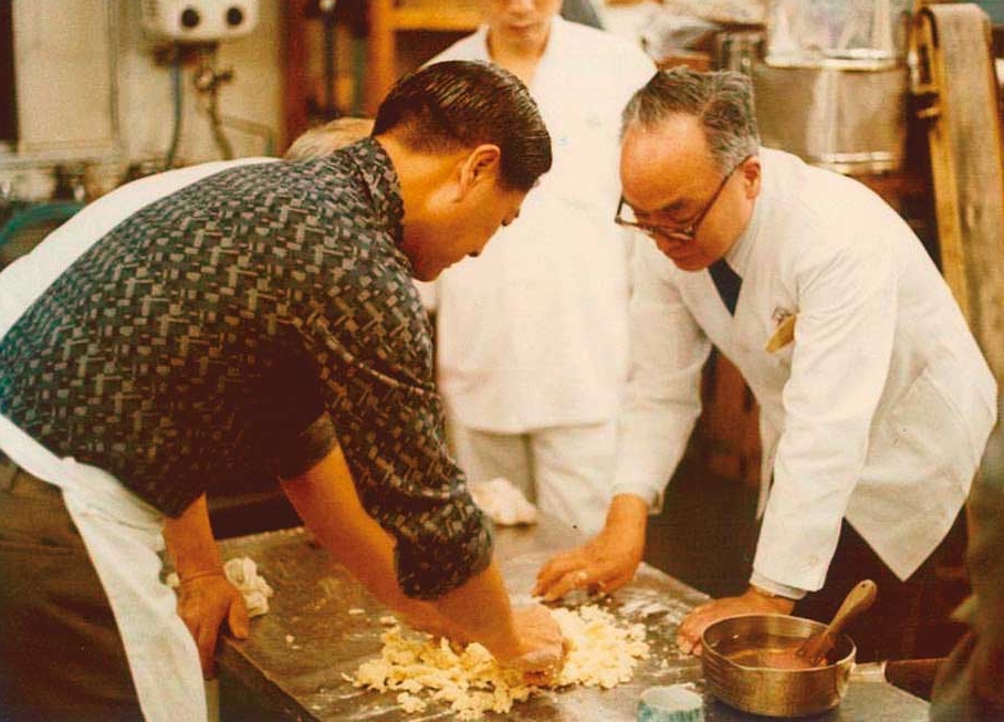 1980年，日本天皇御廚板垣正二（右）到不二家擔任顧問，教導製作蜜紅豆等日式技藝。（不二緻果提供）