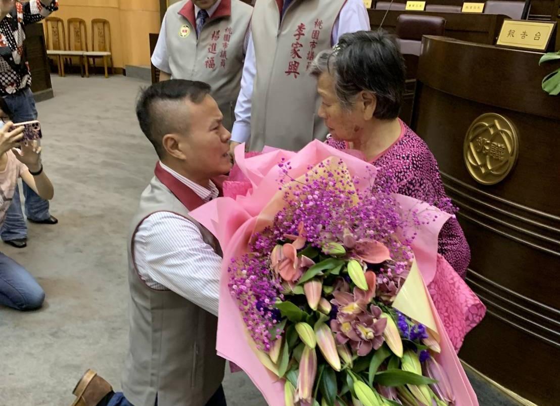 段樹文當選議員後，在議會向高齡母親獻花下跪。（讀者提供）