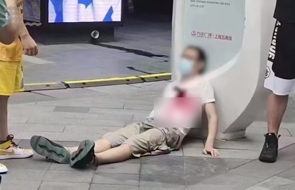 上海萬達廣場一名男子胸口插刀，衣服沾血倒地，引發圍觀。（翻攝新浪新聞影片）