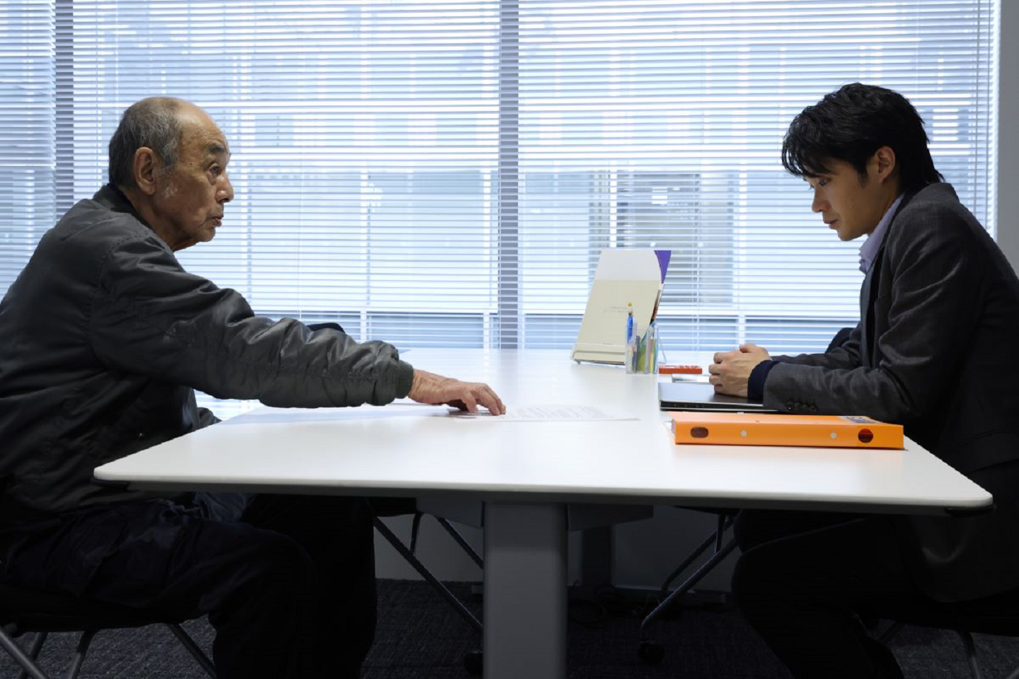 磯村勇斗(右)在《七五計劃》飾演承辦七五計劃的公務人員,卻因遇上親戚申請而有了遲疑。(天馬行空提供)