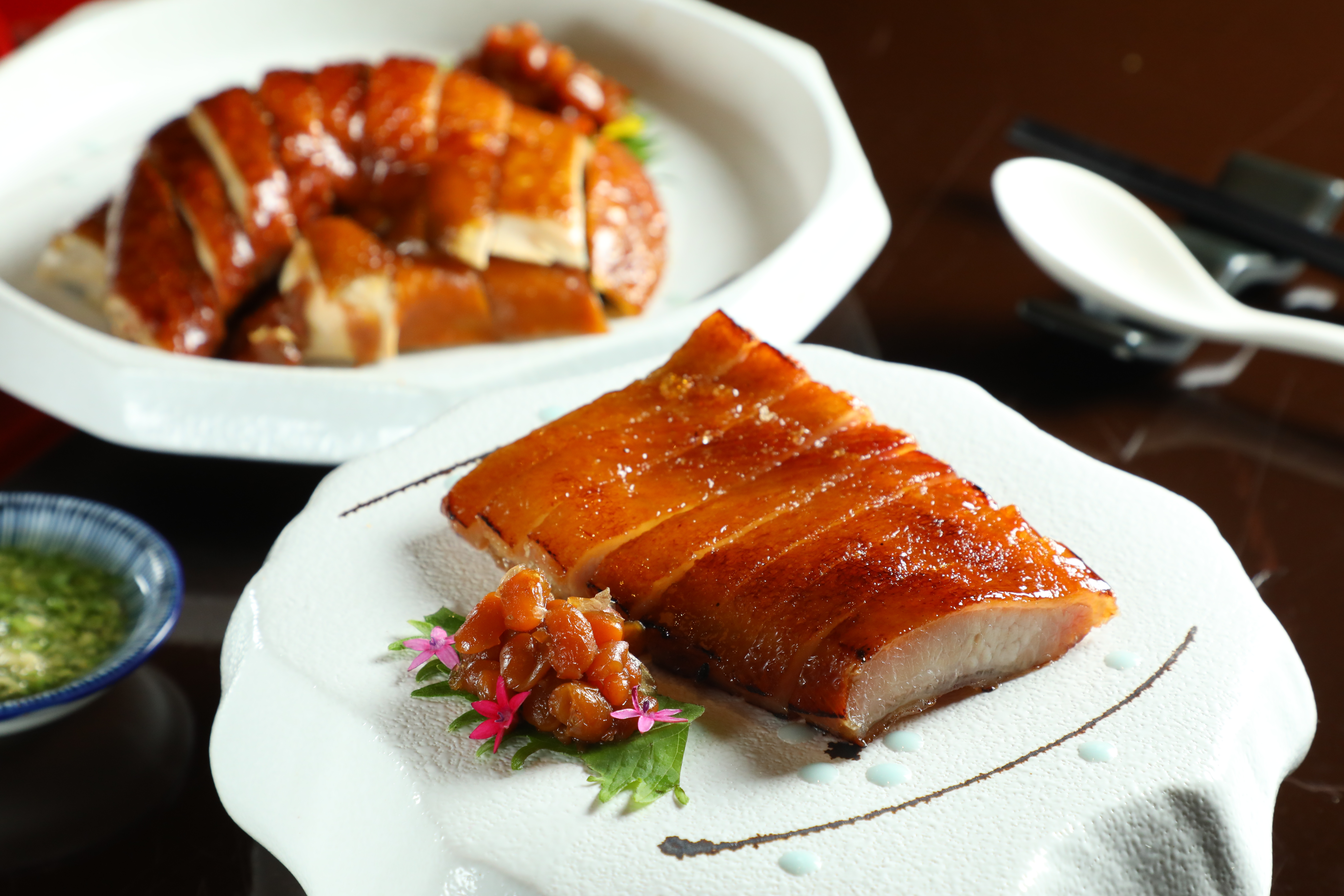 上頭有一層薄薄糖片的「脆皮叉燒」（前，720元／份），曾是辰園的名菜，後方則是玫瑰油雞（後，580元／份）。