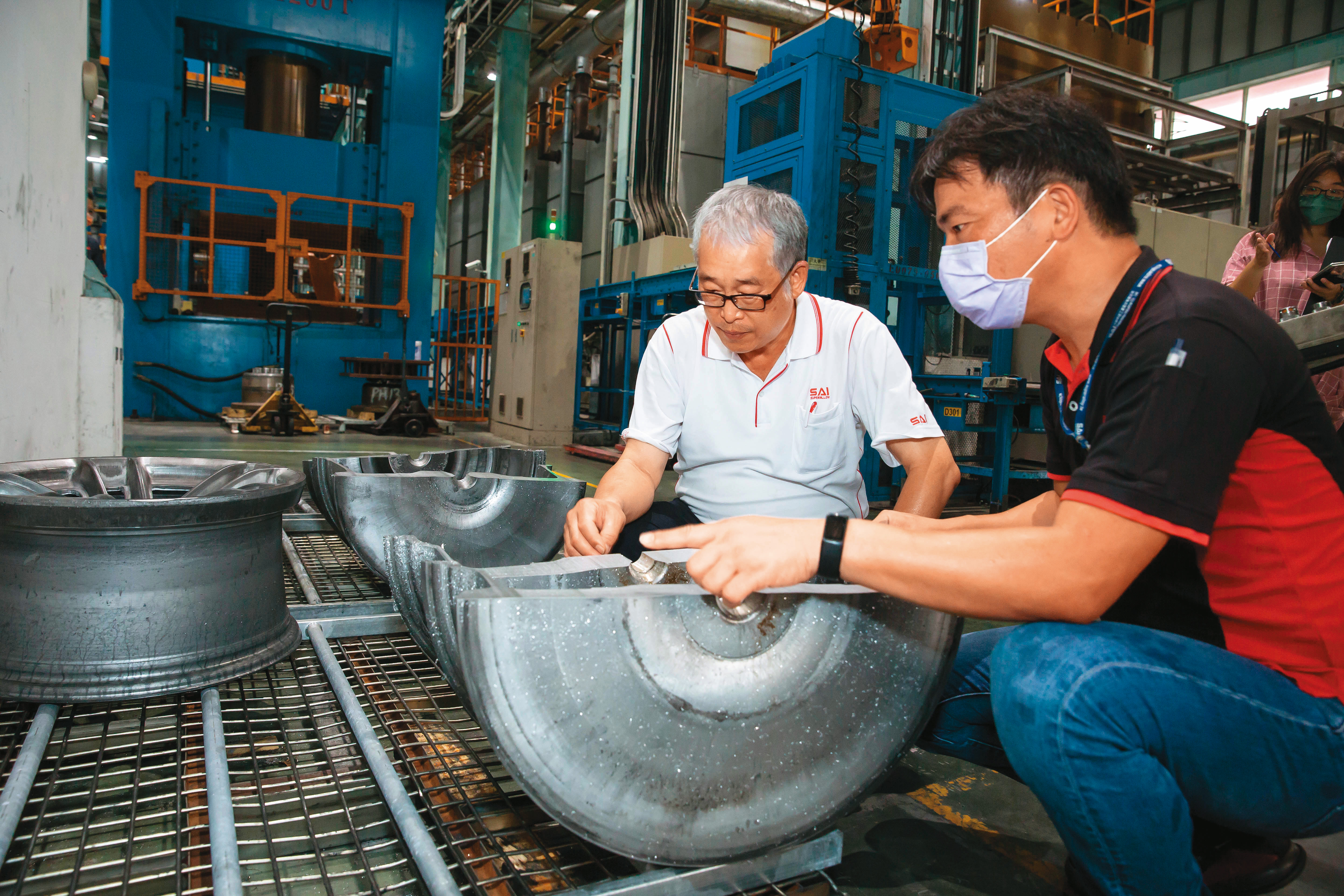 黃聰榮（左）重視製程基本功與細節，巡廠時與員工一起檢查經過粗鍛、細鍛的輪圈厚薄度是否符合設定範圍。