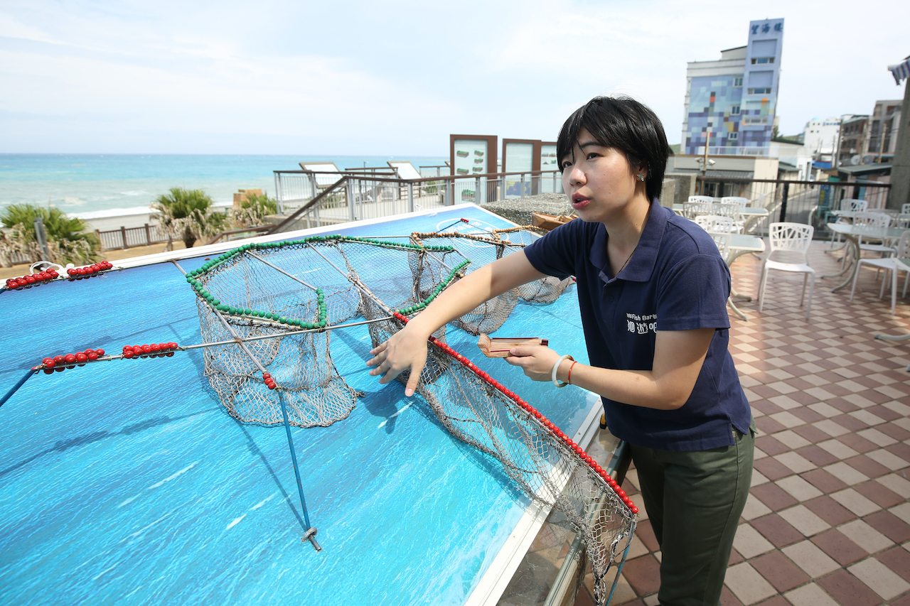 創辦人暨執行長黃紋綺在「洄遊吧」戶外架設一座「定置漁場」教具，正對大海講解友善漁法的重要性。