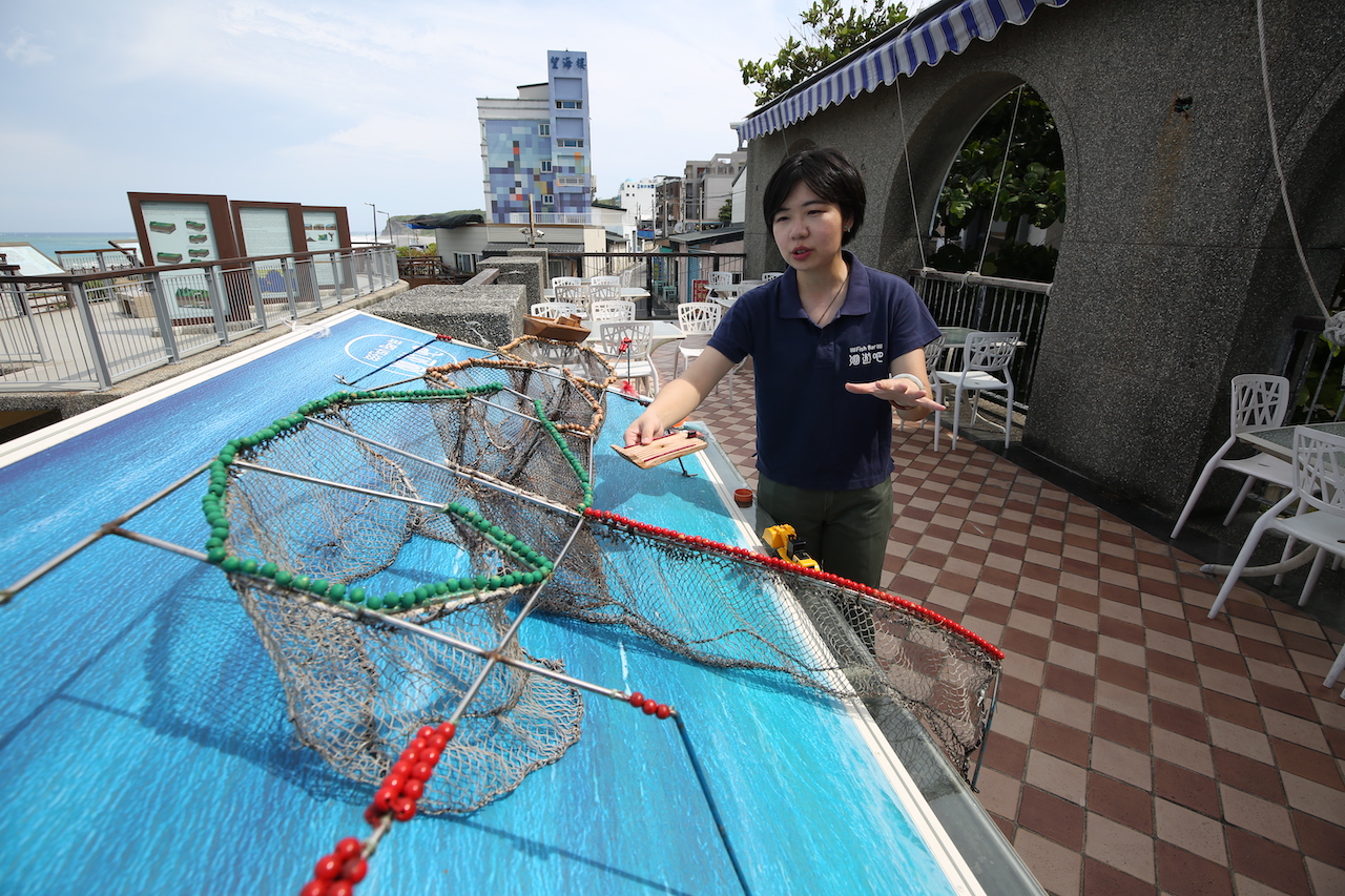 創辦人暨執行長黃紋綺在「洄遊吧」戶外架設一座「定置漁場」教具，正對大海講解友善漁法的重要性。