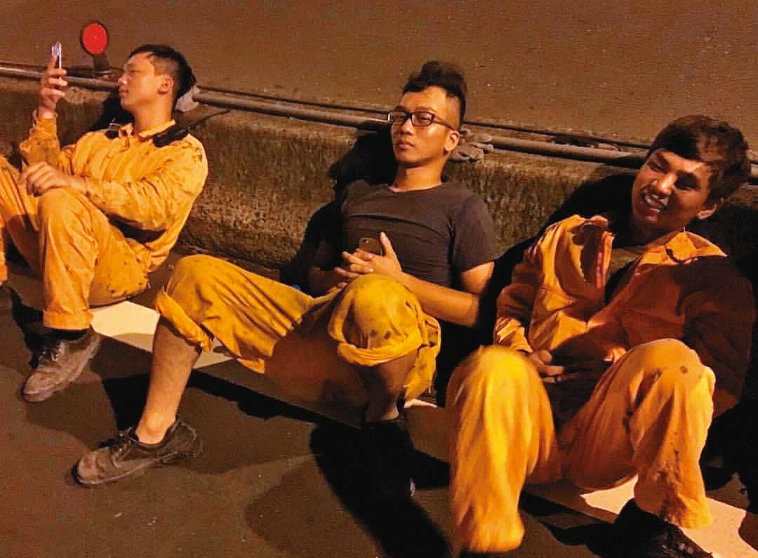 20多歲時的小姜（中）曾是塔吊工人，午夜到工地拆完塔吊台，與同事累坐路邊。（小姜提供）