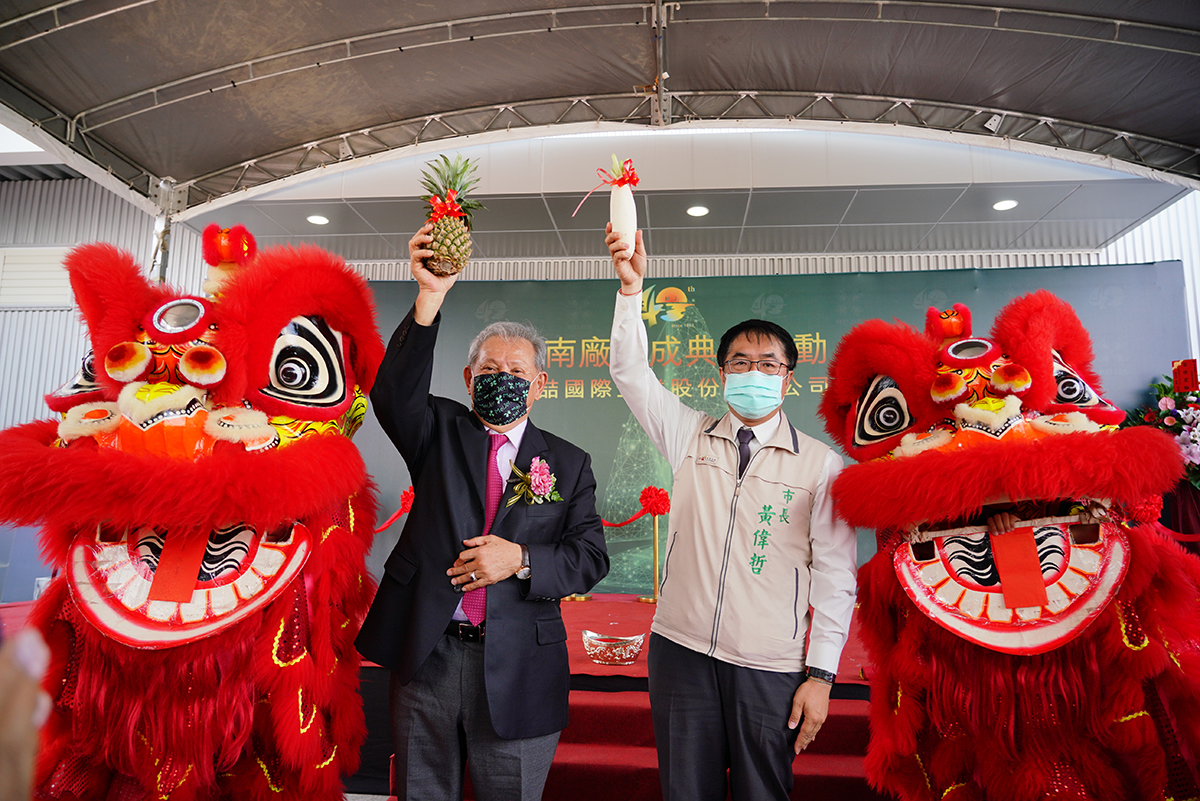 美喆台南新廠落成，董事長陳本源（左）與台南市長黃偉哲高舉鳳梨與菜頭（白蘿蔔）要取得好彩頭。