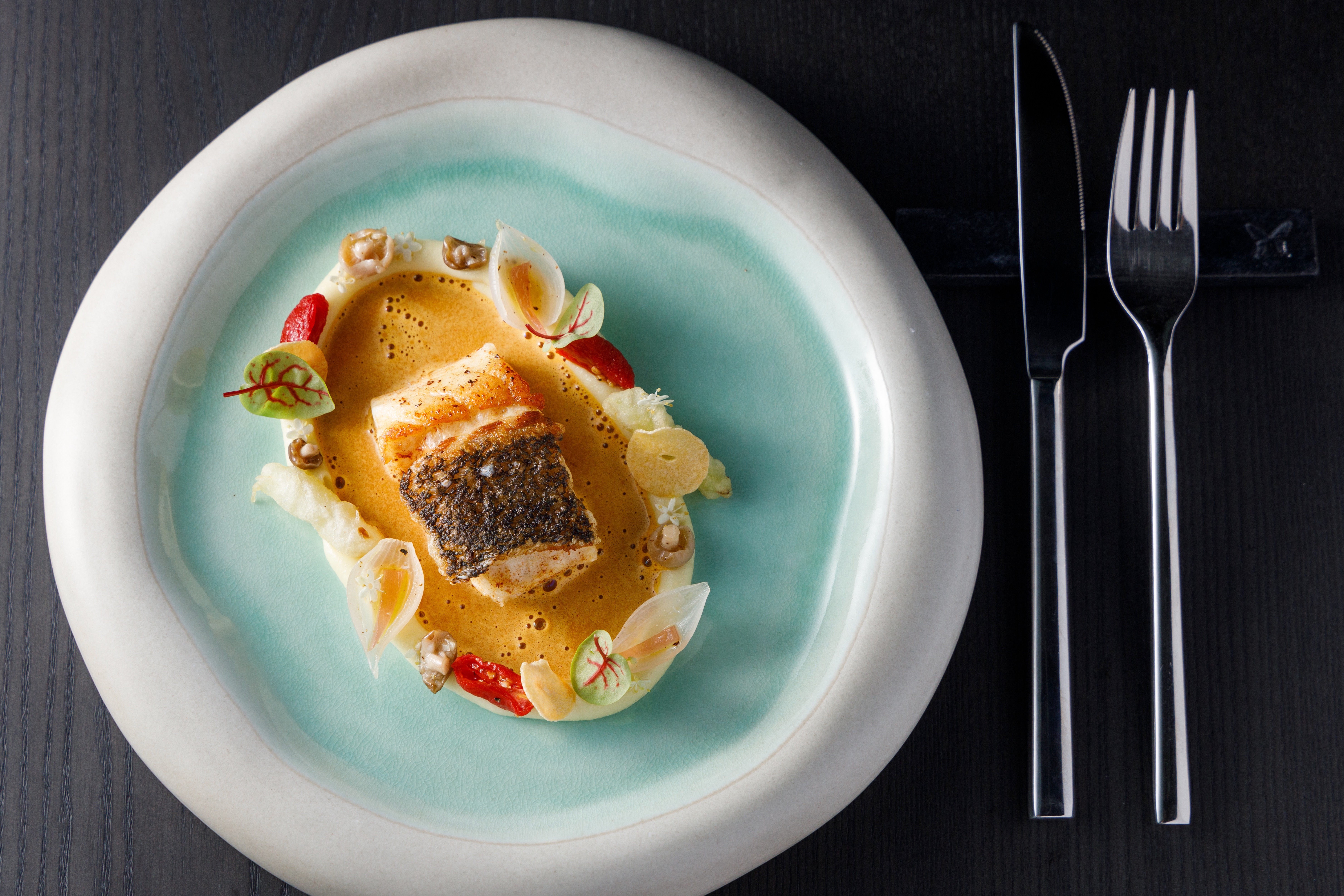 「龍膽石斑、番紅花海鮮高湯」以馬鈴薯泥圍邊裝盛番紅花海鮮高湯，搭配水藍色餐盤，讓龍膽石斑像套上游泳圈，悠遊海裡。