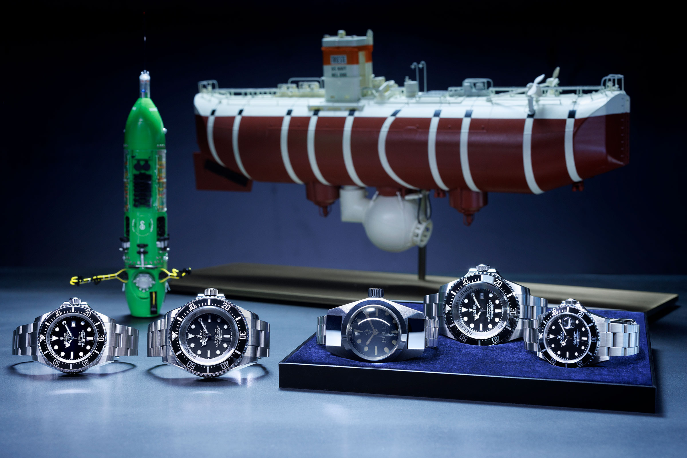(由左至右)Oyster Perpetual Rolex Deepsea(2008)、Oyster Perpetual Deepsea Challenge(2022)、Deep Sea Special(1960)、Rolex Deepsea Challenge(2012)及Oyster Perpetual Submariner(1986)。後方由左至右:深海挑戰者號潛艇及深海潛艇的里雅斯特號的模型。