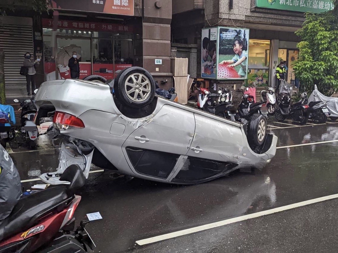 一部轎車因與撞上車門的車輛發生碰撞，導致翻車橫躺路邊。（翻攝畫面）