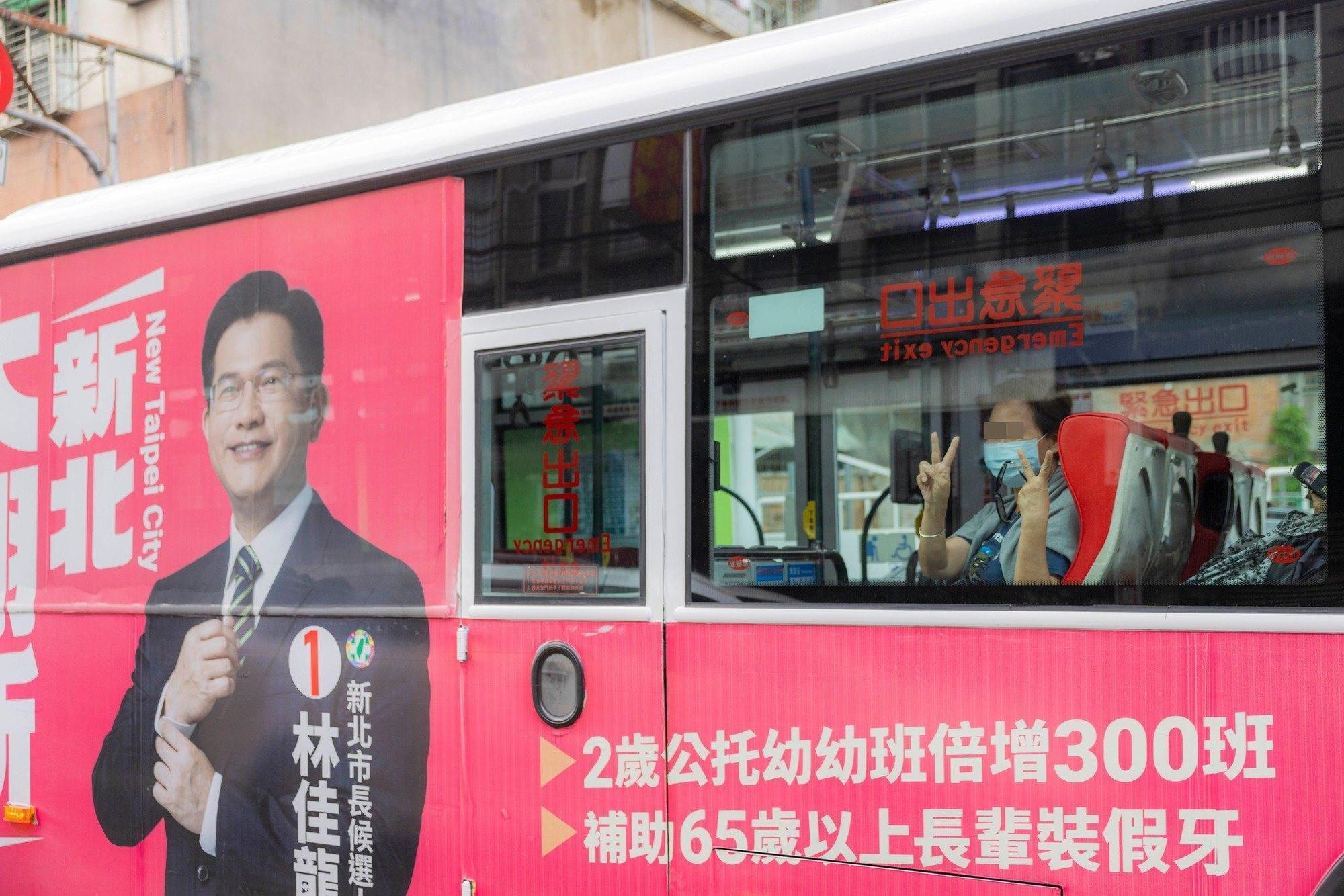 貼有林佳龍競選廣告的公車上，一名婦女手比「2號」手勢，支持侯友宜。（翻攝侯友宜臉書）