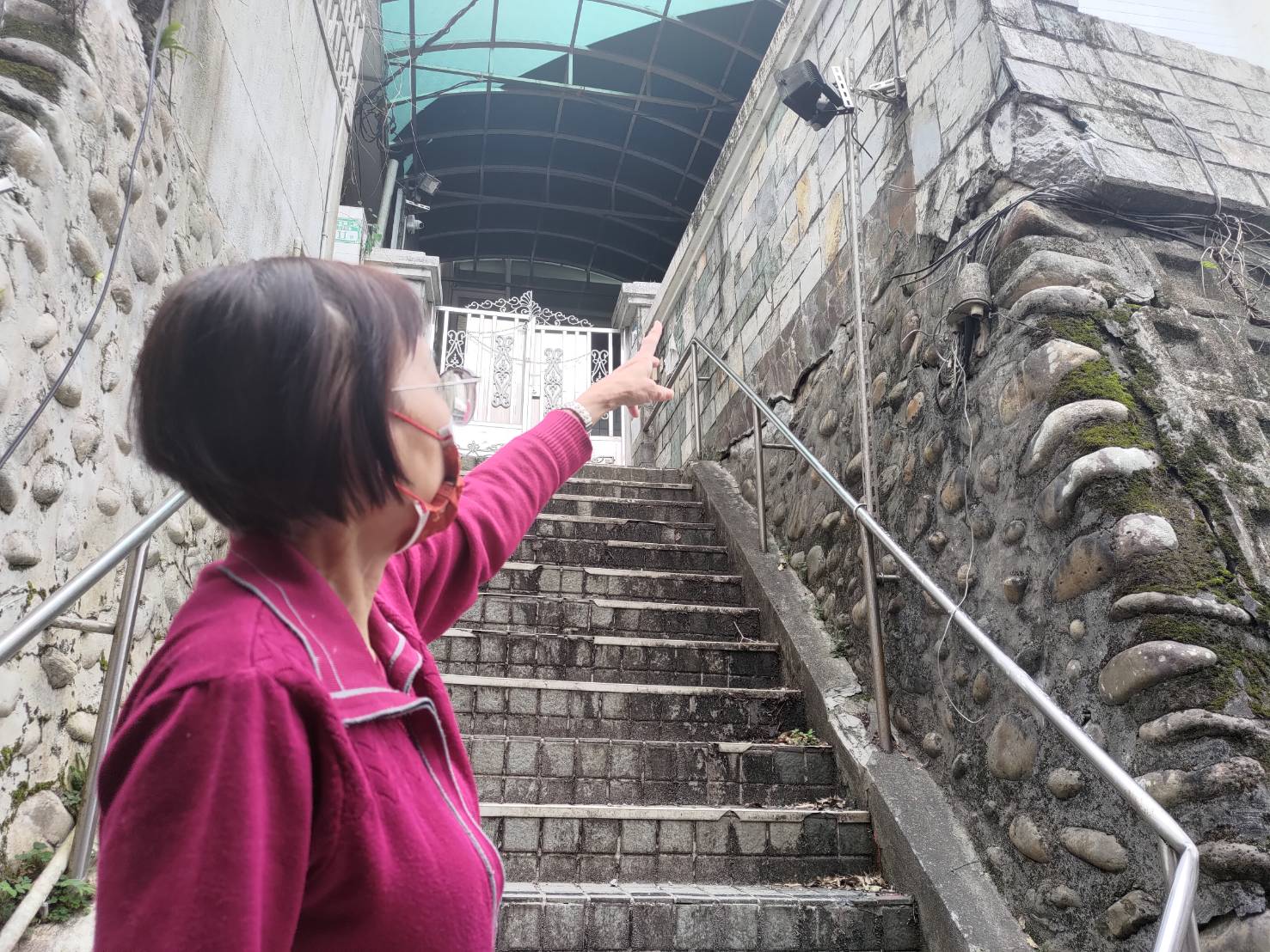 丁婦指著鄰居的建物，指控因其興建駁坎等違建，壓毀自家車庫。