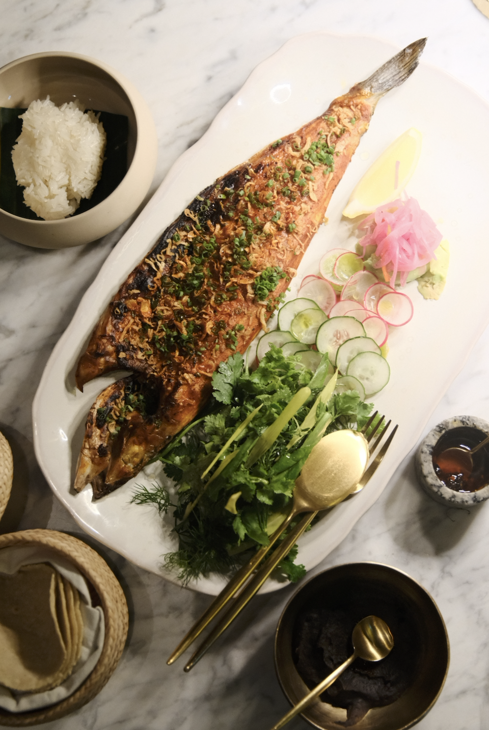 「PESCADO ZARANDEADO」整尾烤魚撒上油蔥、酪梨、阿斗波醬、辣椒等佐料，搭配餅皮一同上桌。（1,500泰銖／份，約NT$1,285）