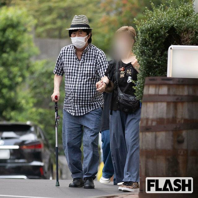 水木一郎(左)今年8月在外受訪後,靠著經紀人攙扶與拐杖緩慢爬坡。(翻攝自《FLASH》週刊)