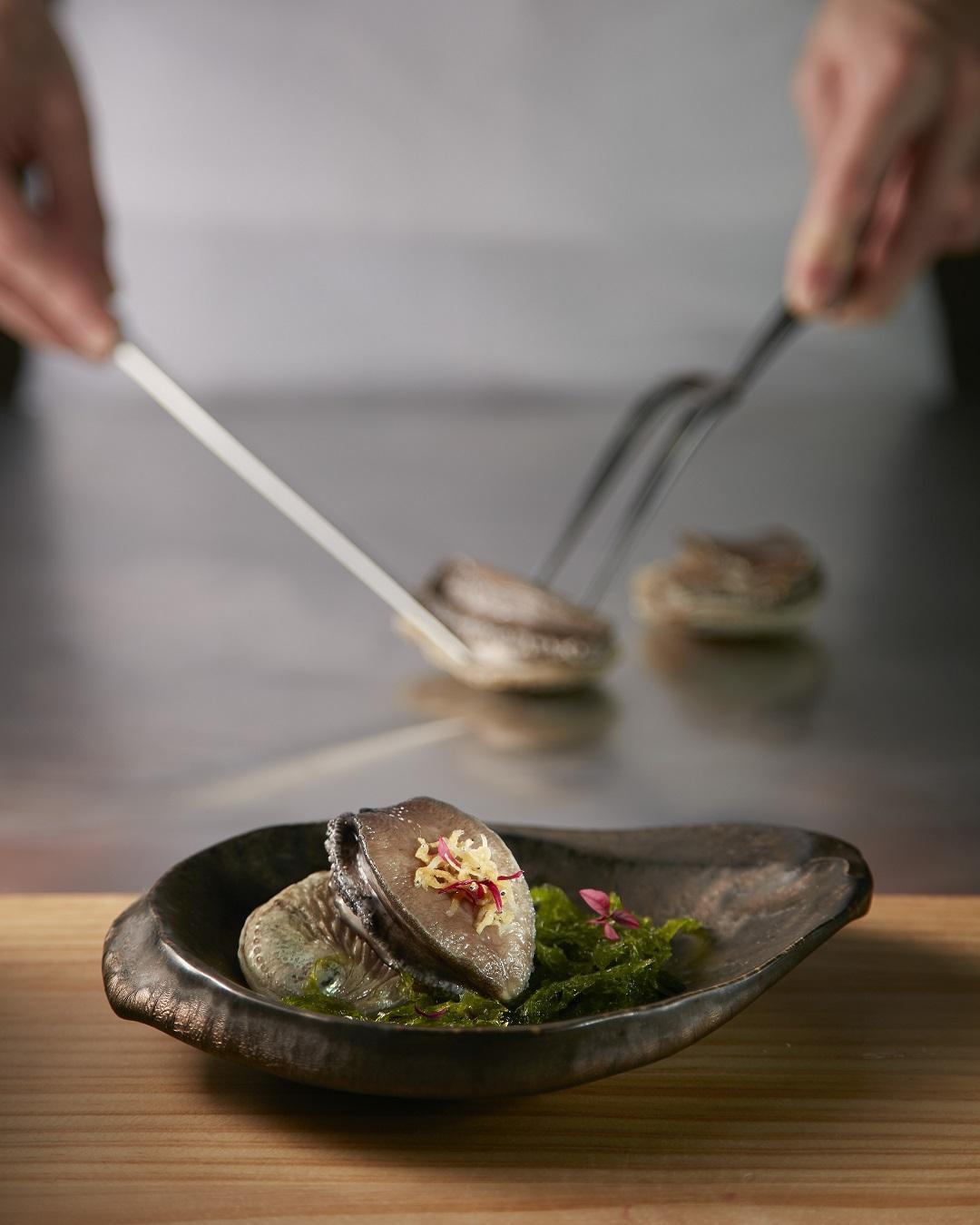 「昆布酒蒸鮑魚」烹調熟度拿捏得宜，肉質彈牙，以紅莧苗、白蘿蔔等擺盤，營造如潮間帶般詩意。（王品提供）