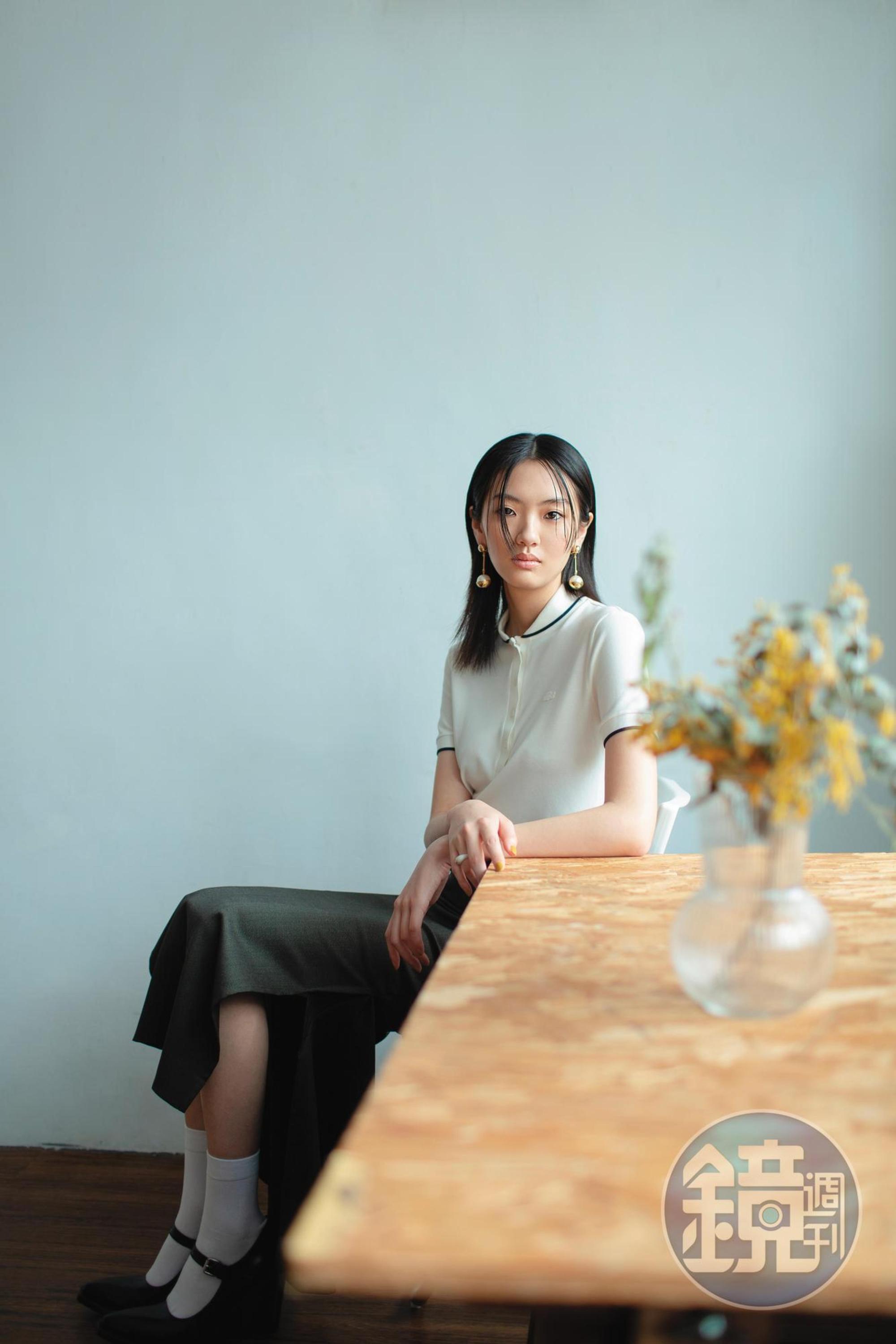 白色飾邊Polo衫 NT$4,880 by LACOSTE／灰色羊毛長裙 NT$23,800 by SPORTMAX／ 黑色尖頭瑪莉珍高跟鞋 價格店洽 by PRADA／珍珠垂墜耳環 NT$18,000 by MIU MIU／白色戒指 價格店洽 by CELINE
