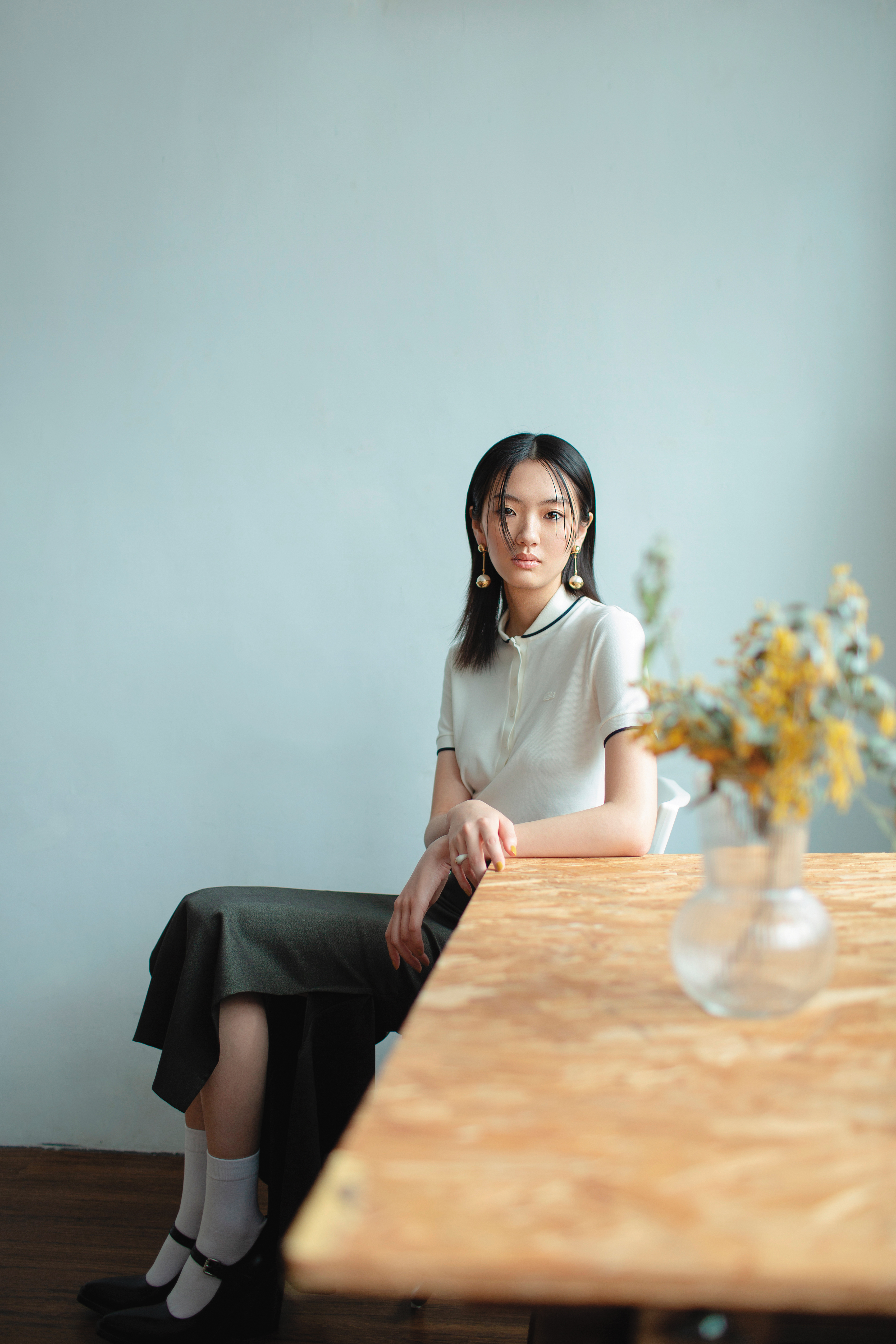 白色飾邊Polo衫 NT$4,880 by LACOSTE／灰色羊毛長裙 NT$23,800 by SPORTMAX／ 黑色尖頭瑪莉珍高跟鞋 價格店洽 by PRADA／珍珠垂墜耳環 NT$18,000 by MIU MIU／白色戒指 價格店洽 by CELINE