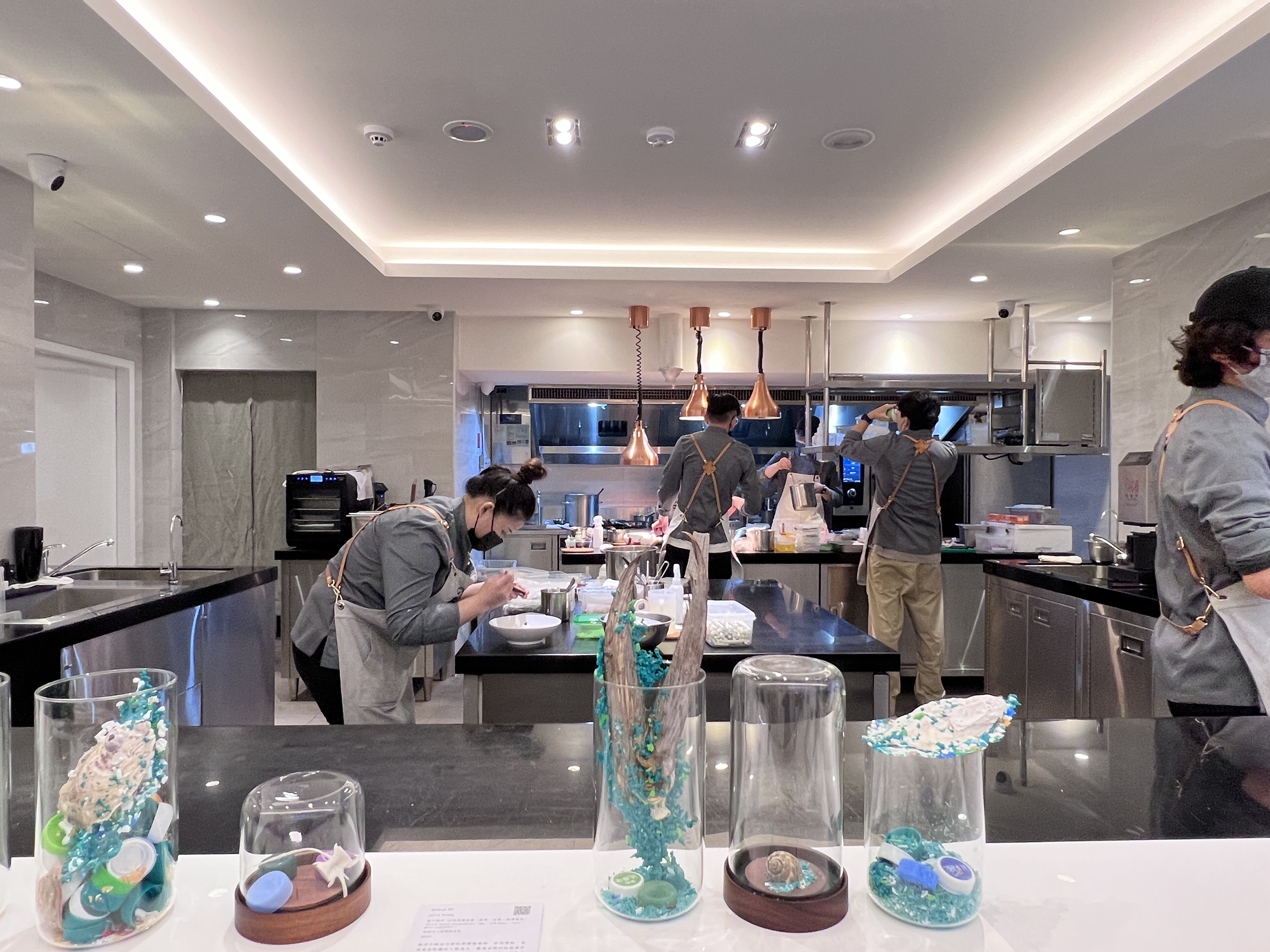 吧台上用魚骨、貝殼結合回收塑料瓶蓋,創作的「化石」作品,後方即是出餐的開放式廚房,友善海洋的心意無所不在。