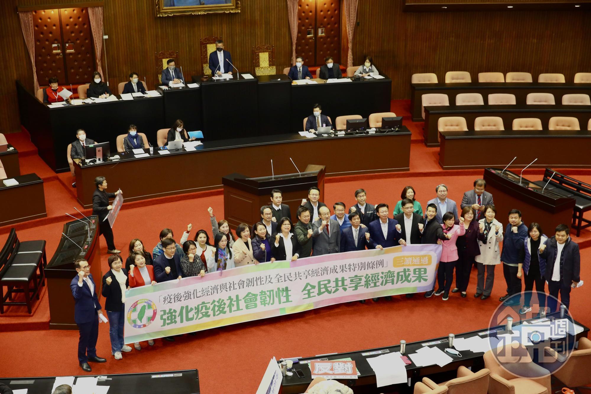 民進黨團高舉「強化疫後社會韌性,全民共享經濟成果」布條,慶祝三讀通過。