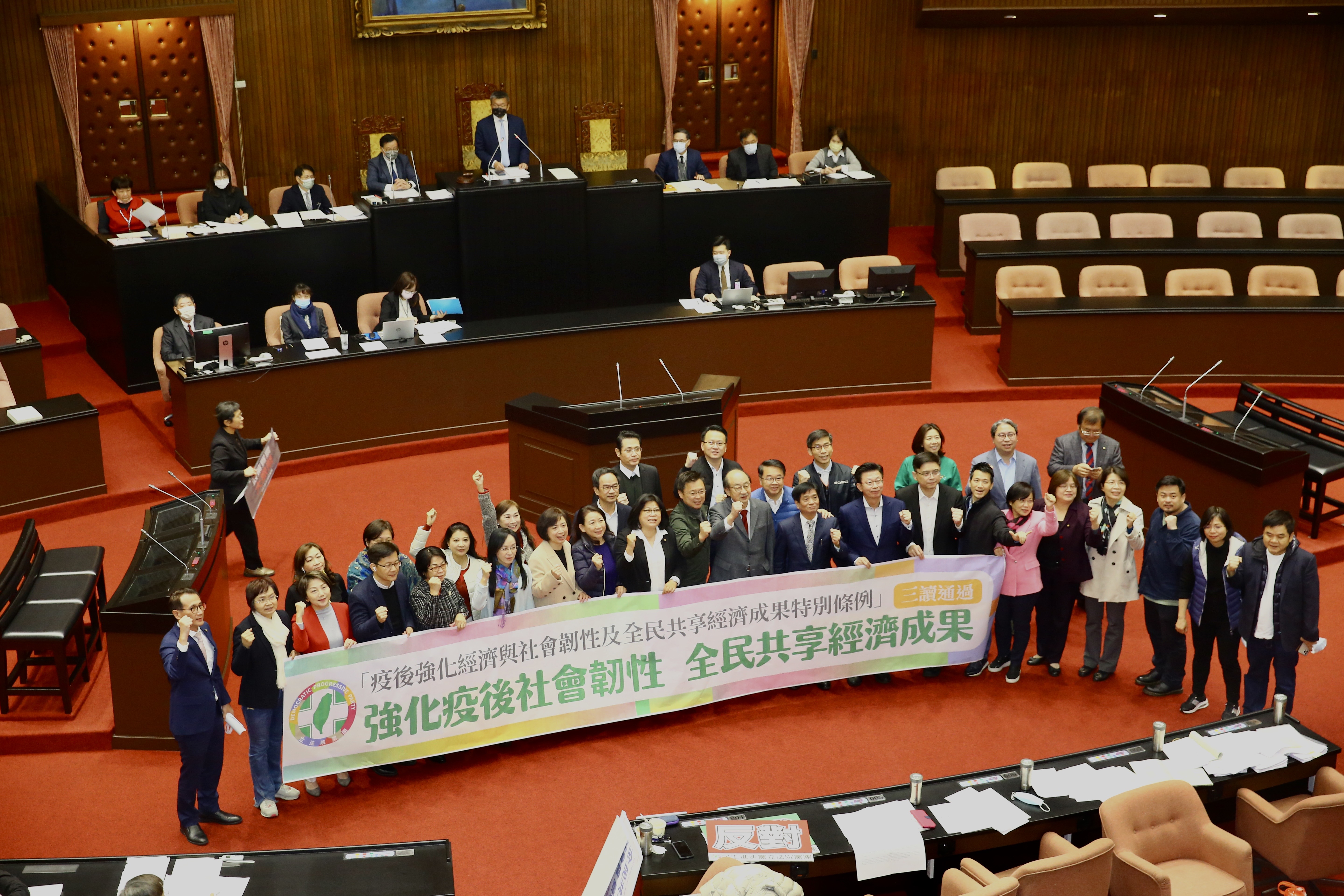 民進黨團高舉「強化疫後社會韌性,全民共享經濟成果」布條,慶祝三讀通過。