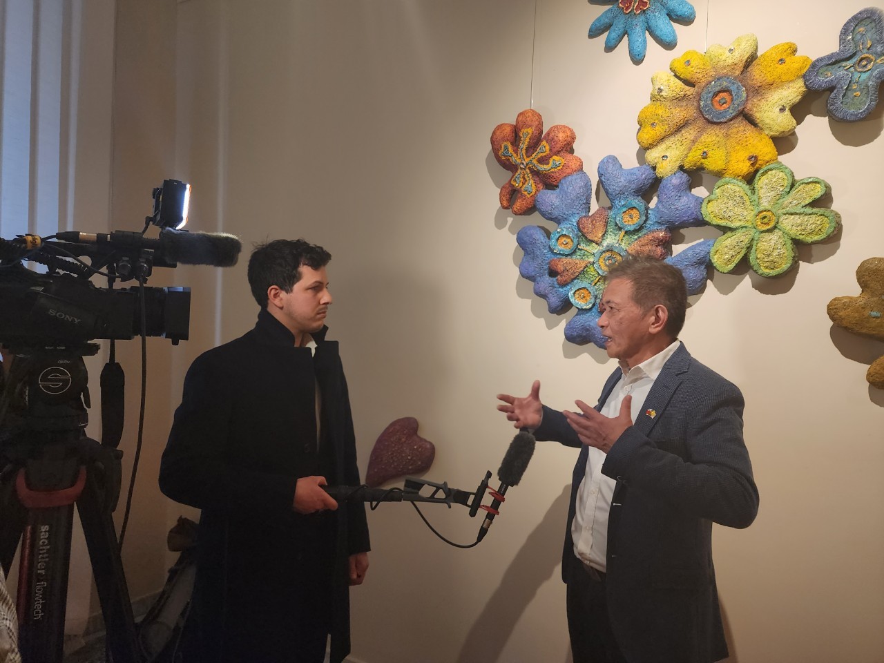 藝術家曾英棟在其作品《繁花似錦》前接受媒體採訪。（甘樂阿舍美術館提供）