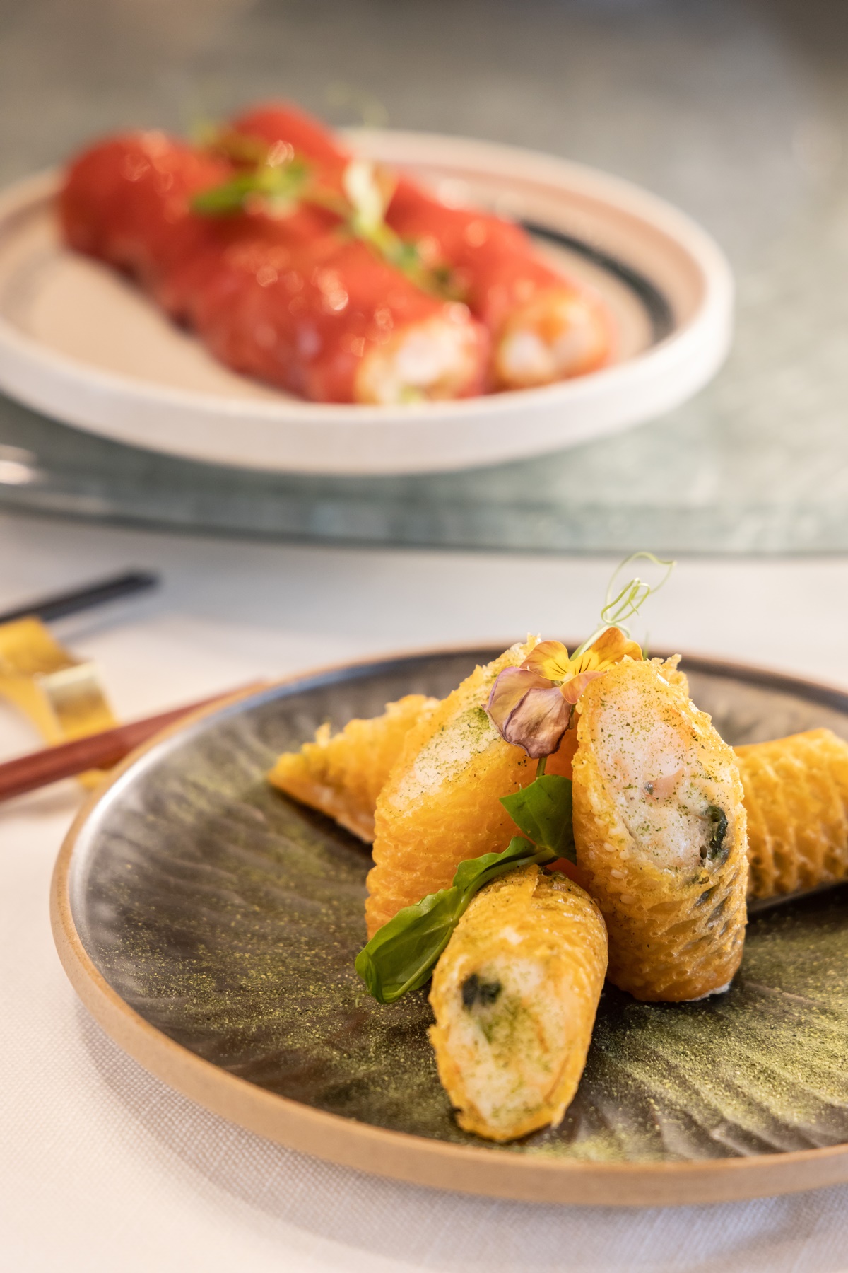 「海苔鱈魚脆春卷」（前，港幣108元／6件）以格子狀的比利時鬆餅皮取代傳統春捲皮；「紅米海皇脆腸粉」（後，港幣108元／2條）用紅米漿攤成腸粉，包裹蝦肉、干貝，爽脆嫩滑，滋味極佳。
