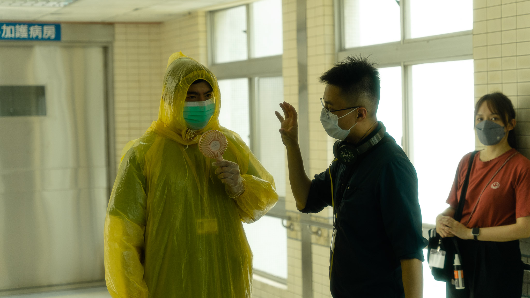飾演醫師的王柏傑(左)穿防護衣全身飆汗,邊吹電扇、邊和導演林君陽(右)討論。 (CatchPlay提供)