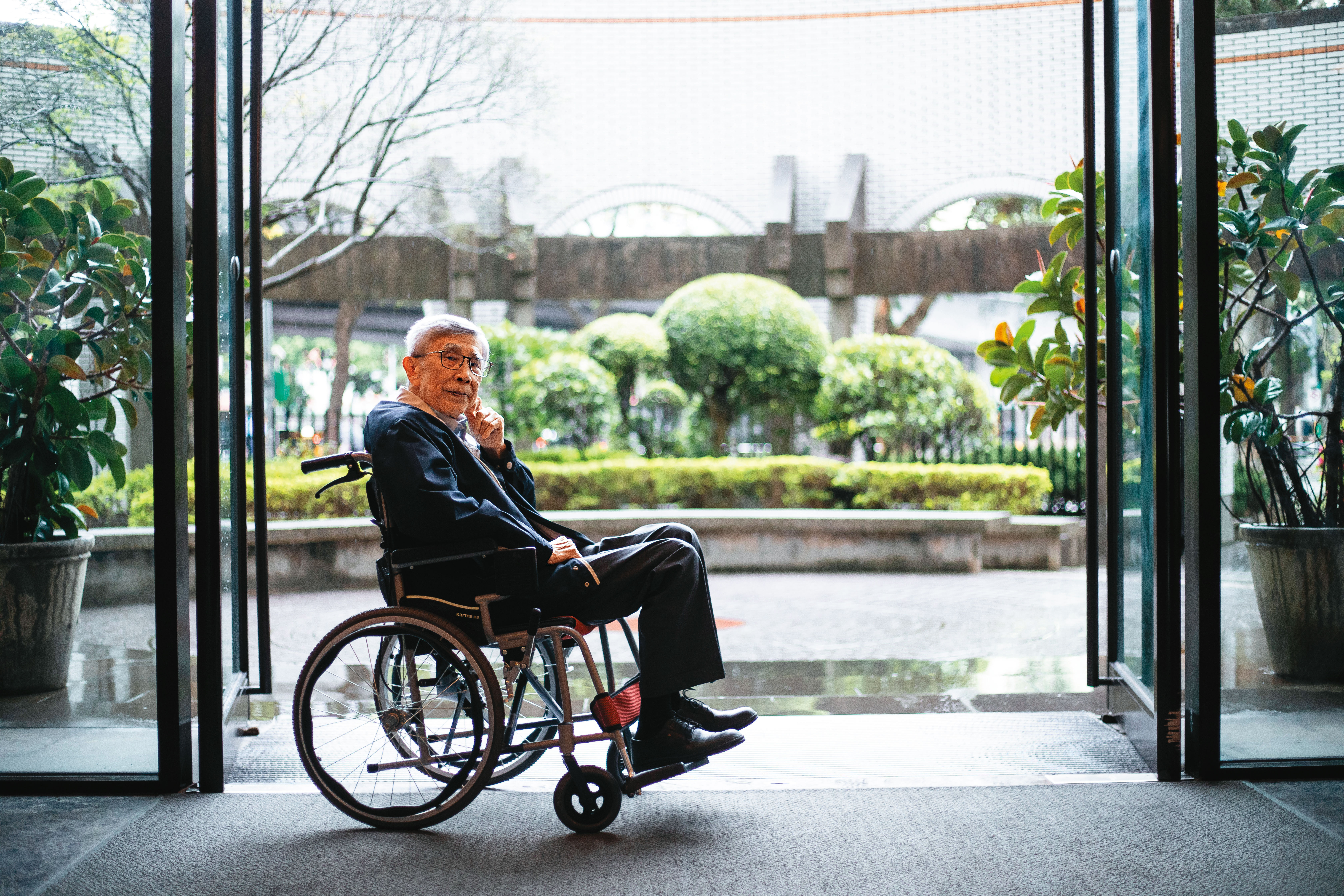 李明亮有種隨遇而安的自在， 初訪時遇雨，他將隨身的拐杖交付記者， 任我們推動輪椅到社區大門口拍照。