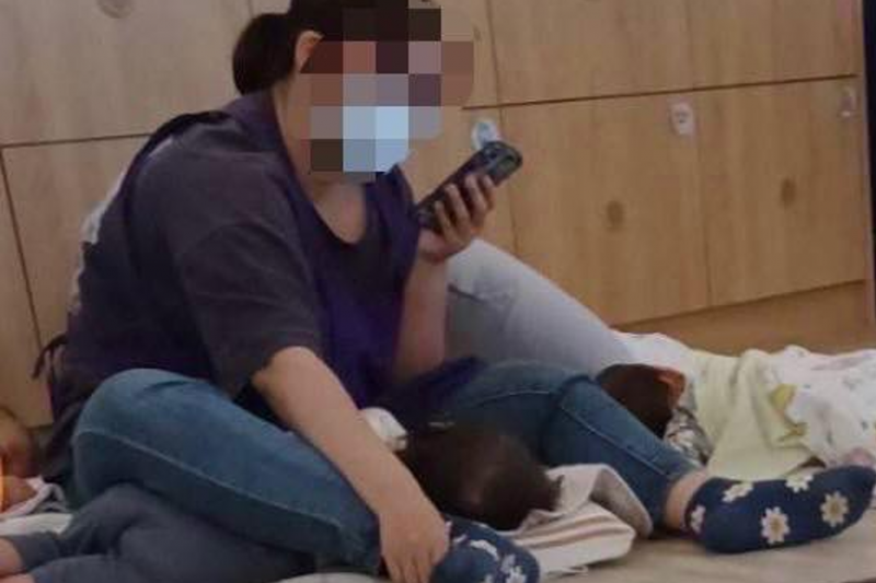 幼保員被拍下邊看機邊用雙腿強行壓制幼童的畫面，引起公憤。（翻攝畫面）