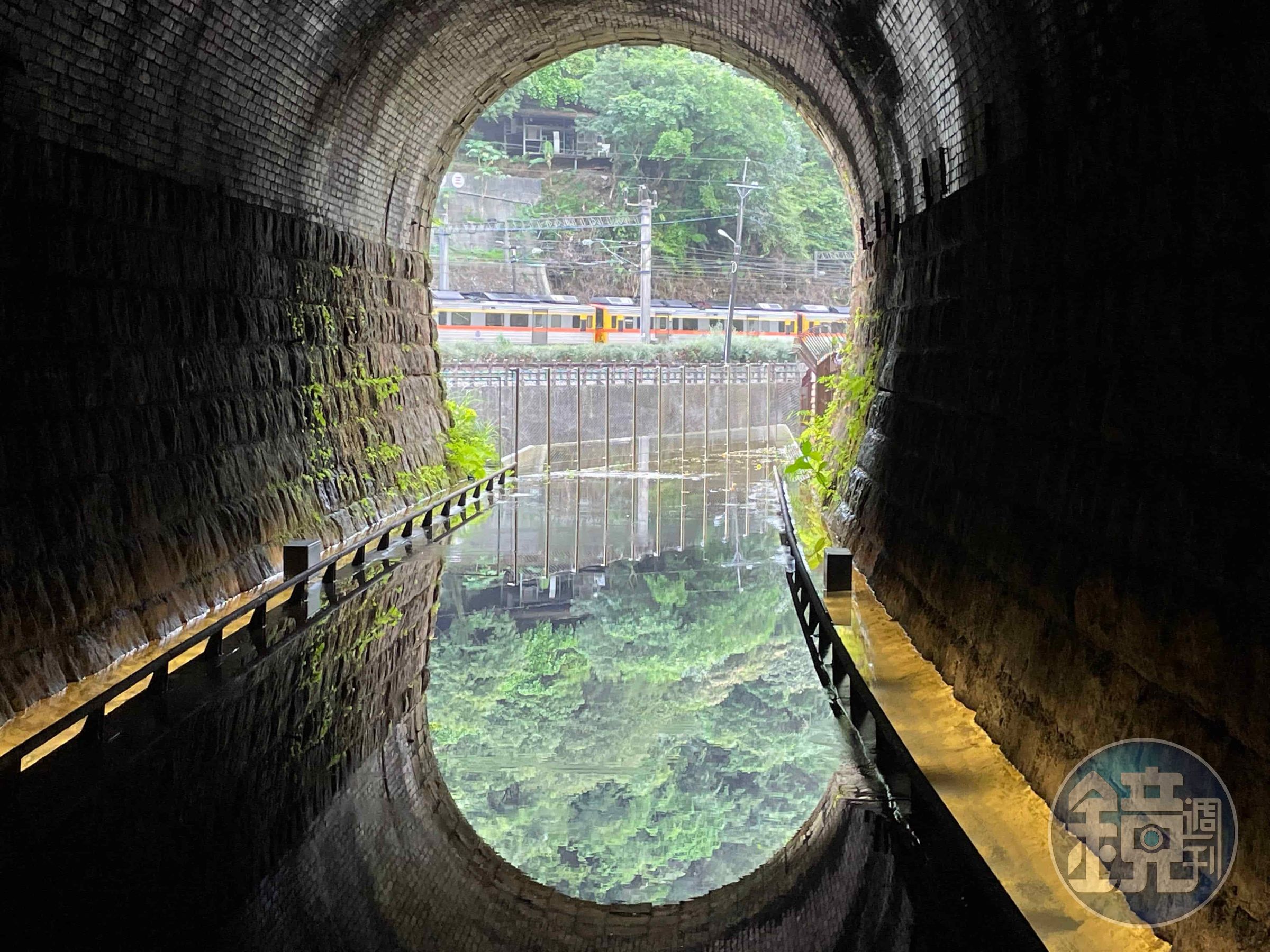 在三爪子隧道設計的鏡面水池反射出翠綠山色及火車行經影像。(新北市觀旅局提供)