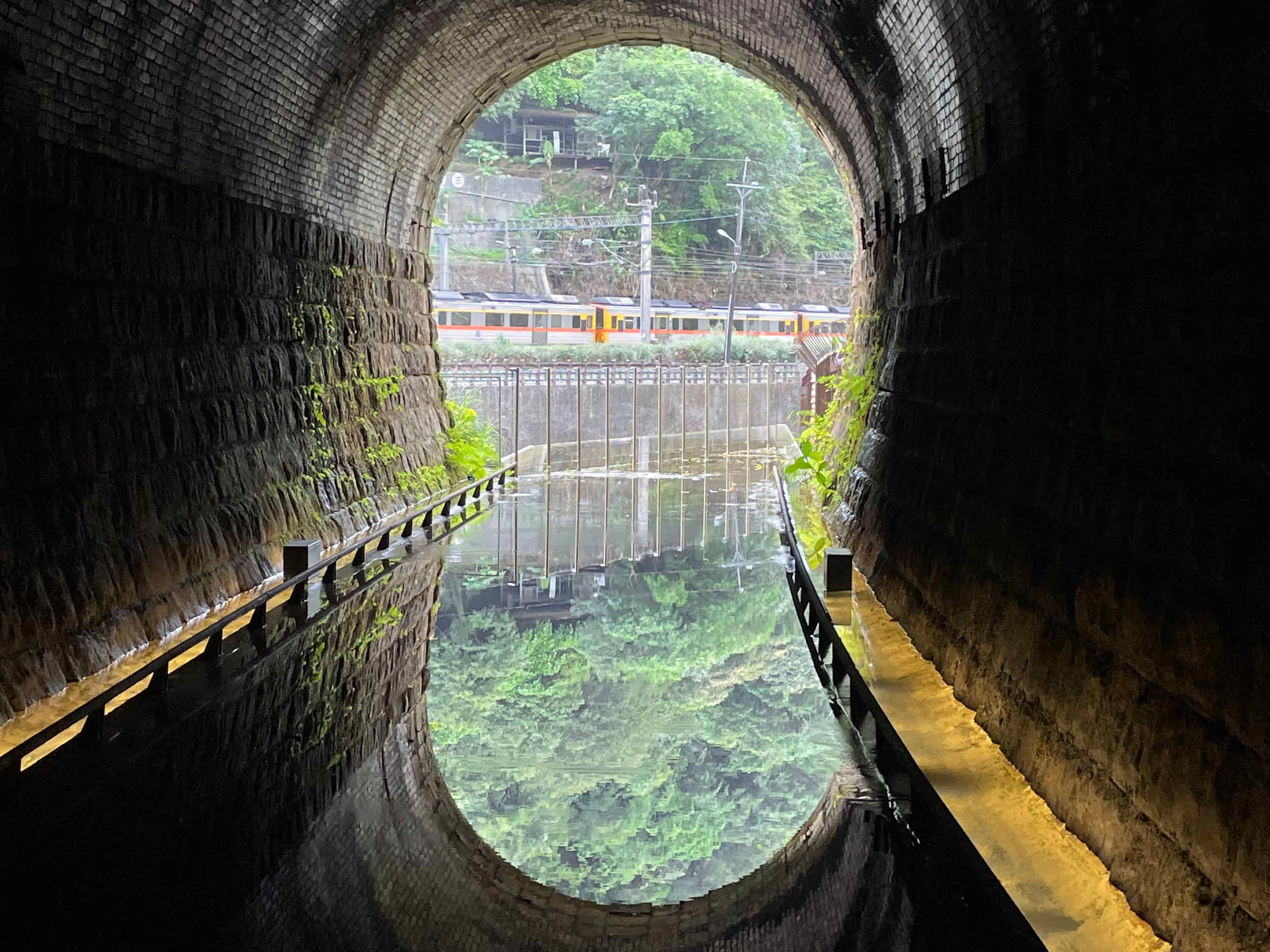 在三爪子隧道設計的鏡面水池反射出翠綠山色及火車行經影像。(新北市觀旅局提供)