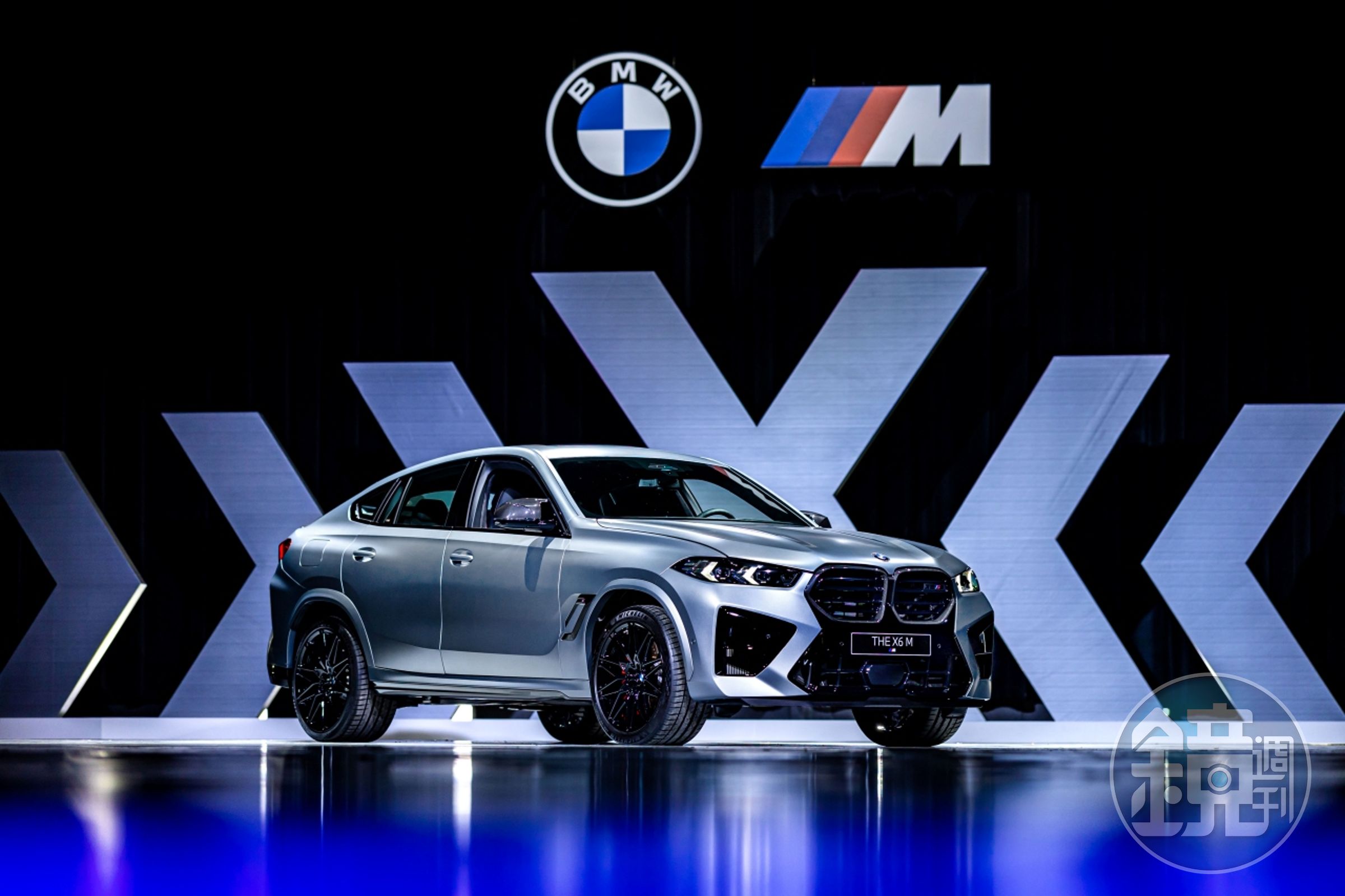 全新BMW X6 M Competition配備M空力套件、燻黑造型光型變化智慧LED頭燈與M碳纖維水箱護罩，結合前保桿下方與兩側的黑色高光澤進氣口造型，展現更強烈的侵略性與辨識度，熱血激昂氛圍溢於言表。