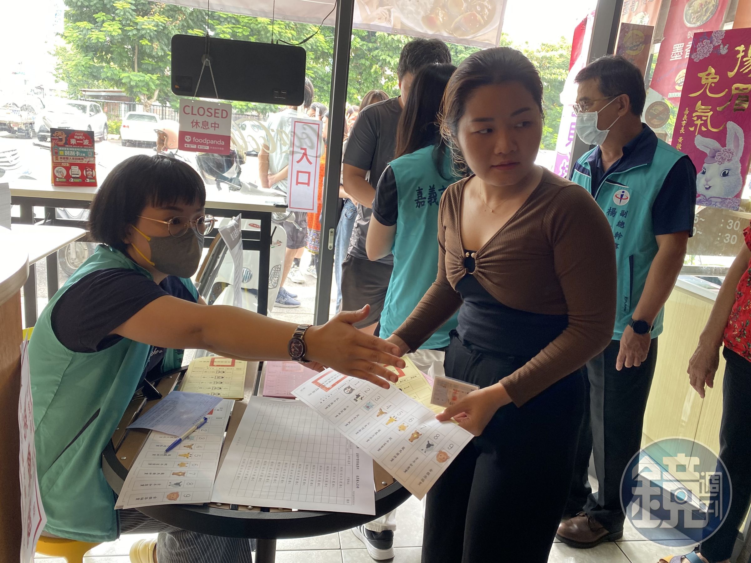 越南新住民紅青(右1)領取模擬選票後,在嘉義市選舉委員會人員引導下,前往圈票處模擬圈選心目中的候選人。(移民署嘉義市服務站提供)