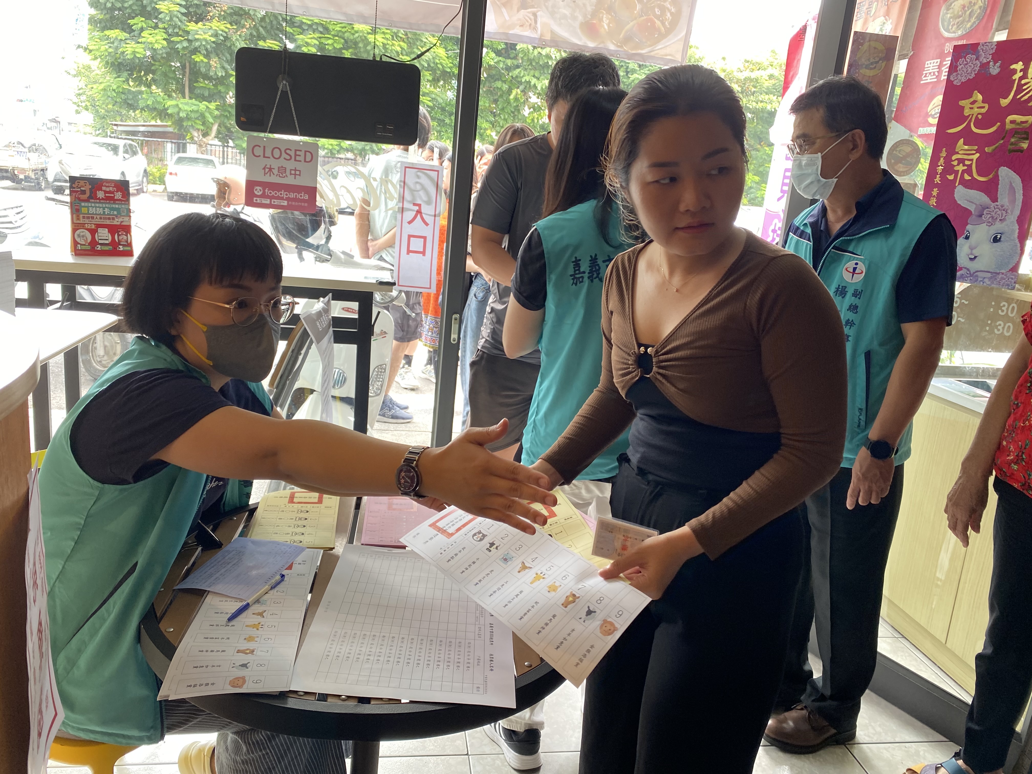 越南新住民紅青（右1）領取模擬選票後，在嘉義市選舉委員會人員引導下，前往圈票處模擬圈選心目中的候選人。（移民署嘉義市服務站提供）