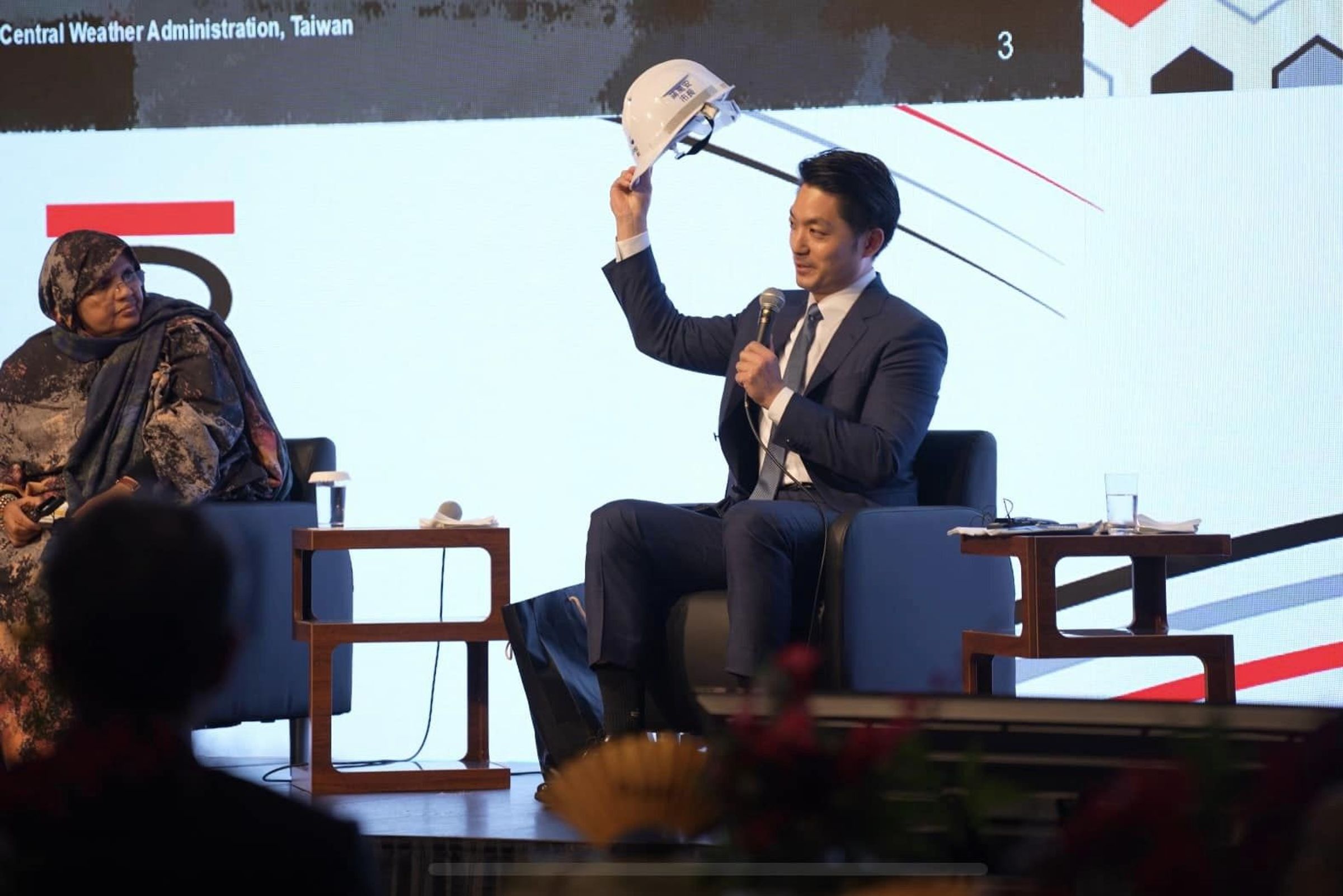 蔣萬安在SusHITech論壇開幕式上短講,拿出防災背心、頭盔,分享台北市的防災經驗。(台北市政府提供)