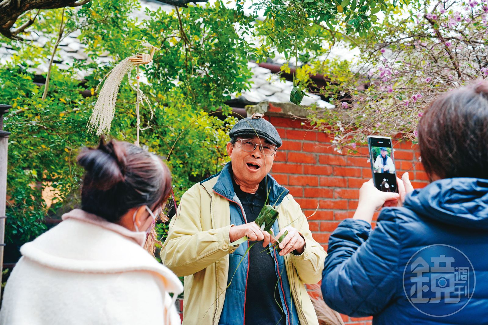 林三元（中）在街頭進行草編創作時，會與遊客熱烈互動，讓人忍不住拿起手機記錄過程。（圖／鏡週刊）