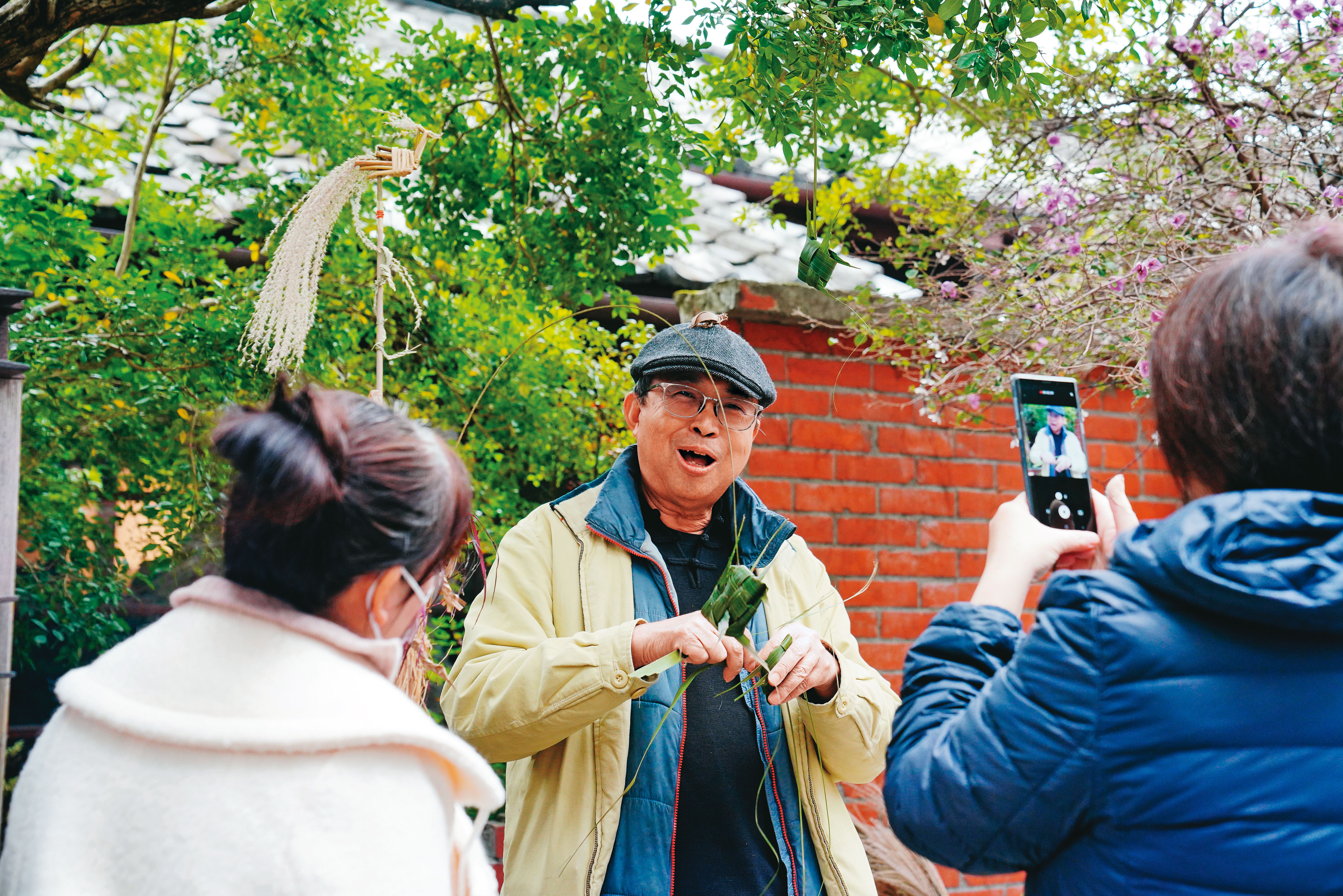 林三元（中）在街頭進行草編創作時，會與遊客熱烈互動，讓人忍不住拿起手機記錄過程。