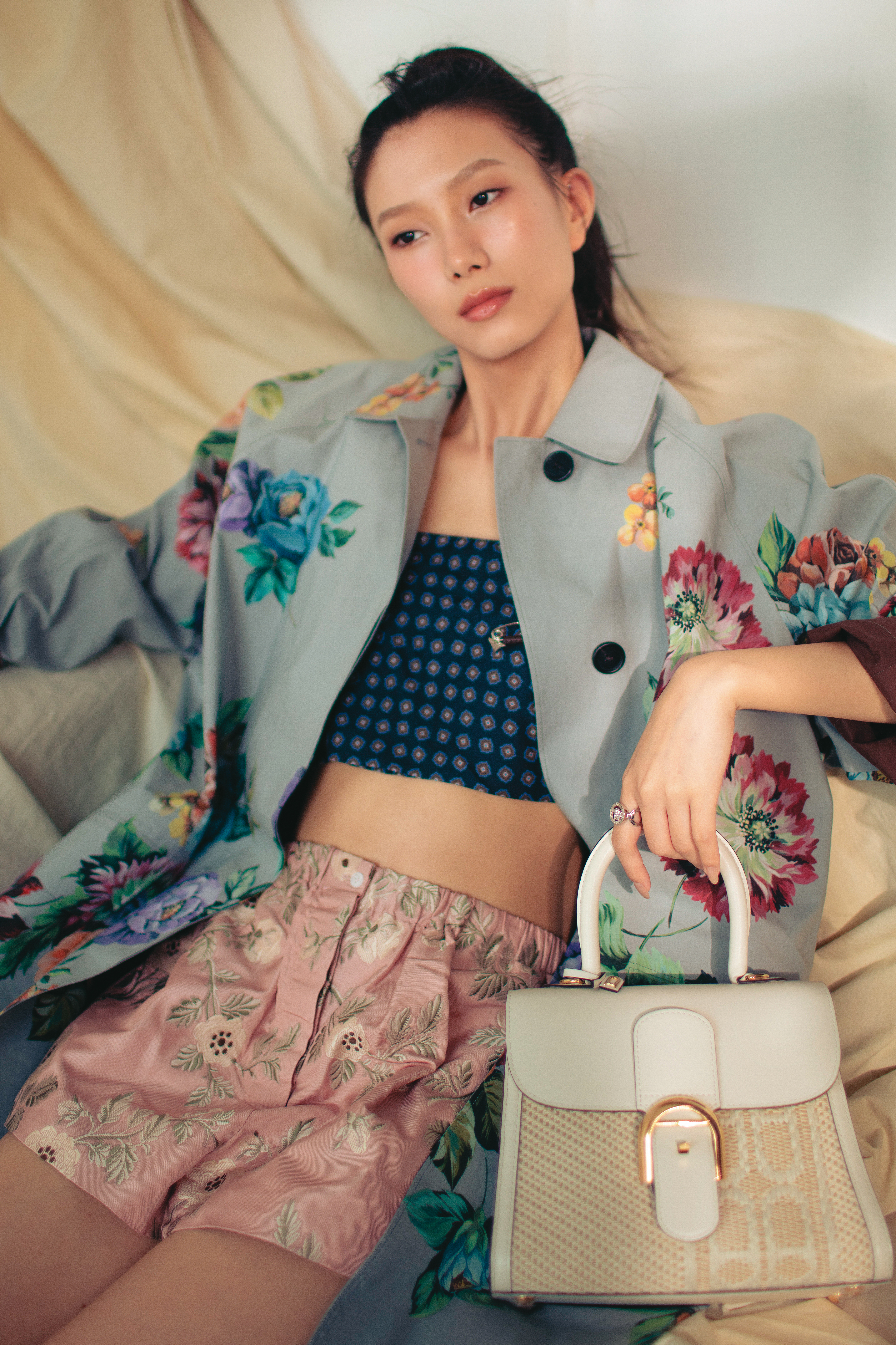 燕麥色與象牙白Brillant PM Versus Jacquard Illusion包款 NT$226,400 by DELVAUX／灰色花卉風衣 價格店洽 by PRADA／深藍色印花細肩帶上衣 價格店洽 by PRADA／粉色花卉短褲 價格店洽 by PRADA／Medusa '95水晶戒指 NT$12,000 by VERSACE