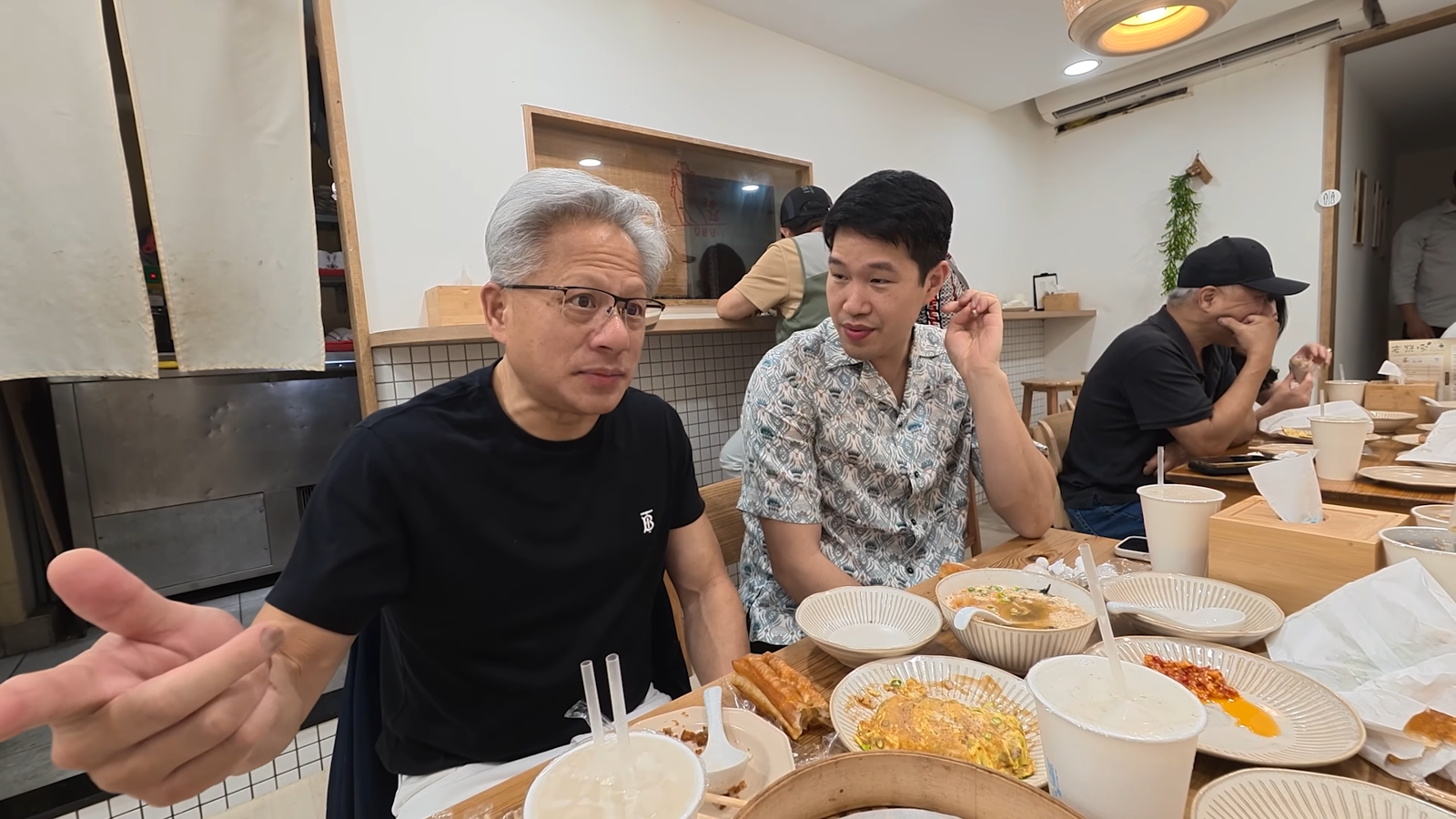黃仁勳（左）一邊享用台灣美食，一邊向眾人分享當年如何透過黃頁電話簿聯絡台積電，展開與張忠謀的合作緣分。（翻攝Lex Fridman YouTube）