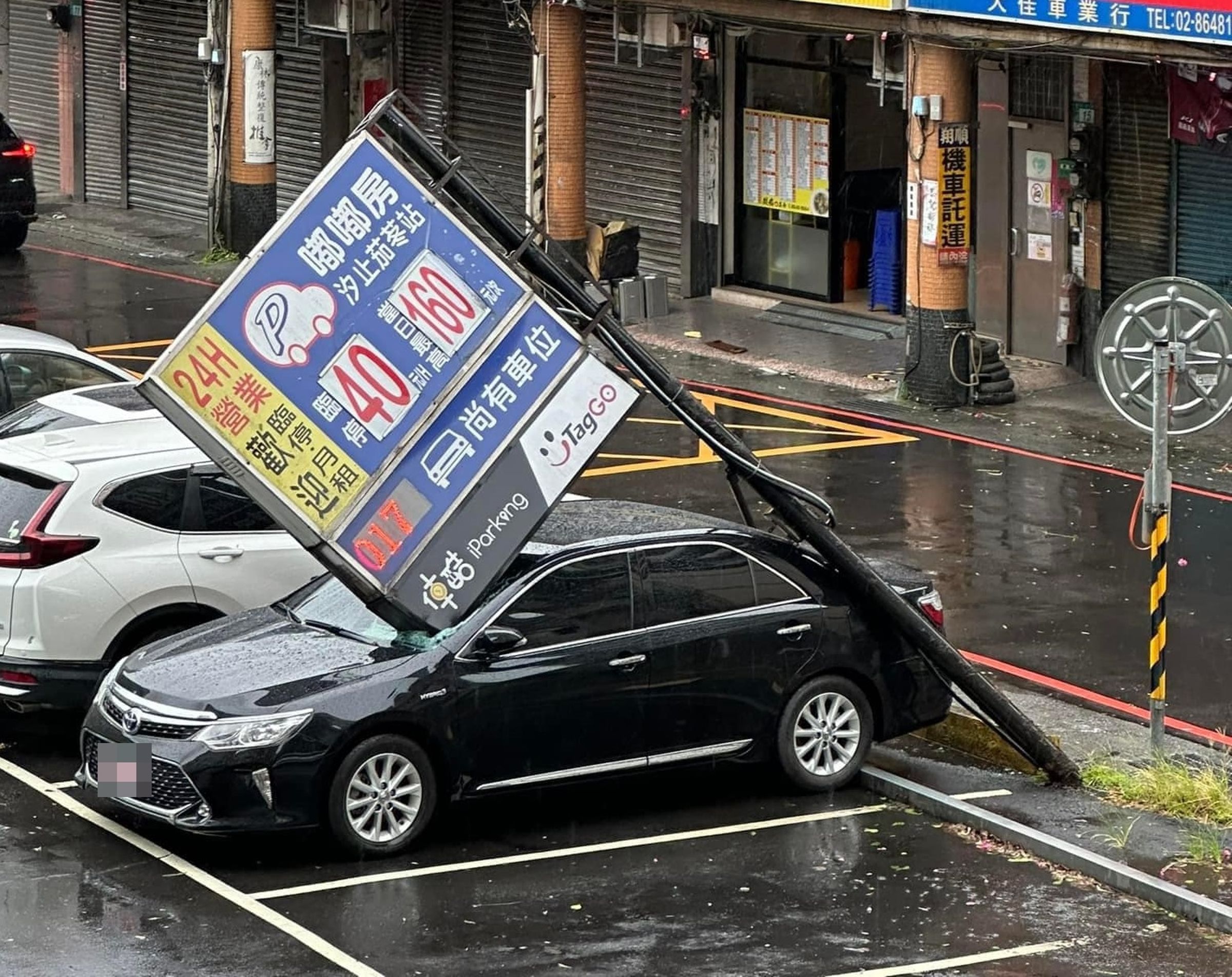 汐止一處停車場的招牌疑似被颱風吹倒,恰巧壓在一台黑色豐田多元計程車上。(翻攝自爆料公社二社)