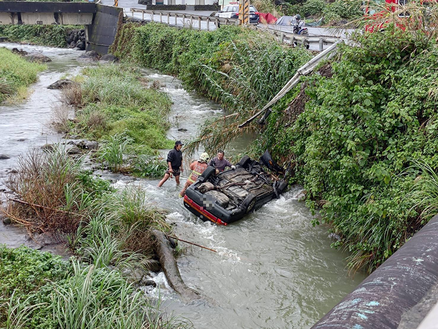 一輛自小客今日上午在貢寮區和美街墜落溪床，整輛車翻覆浸泡在急流中。（翻攝畫面）