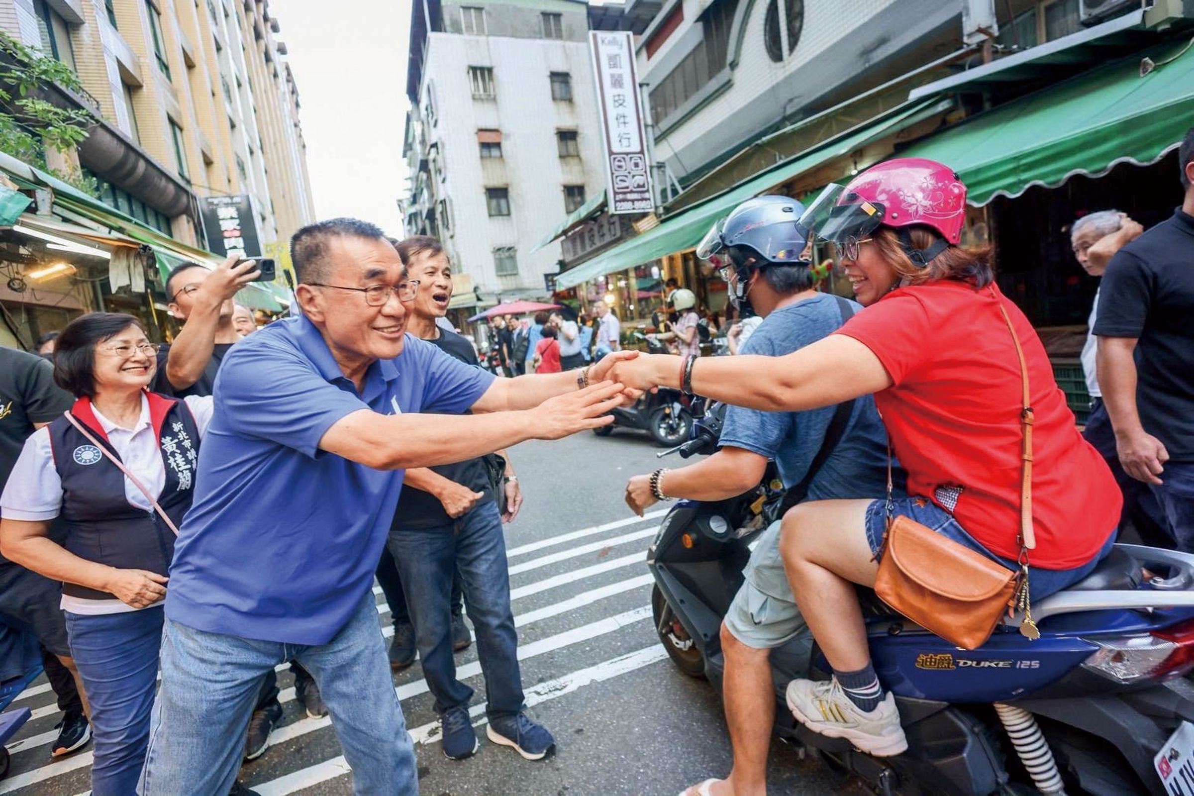 李四川(前左)親自走入街頭拜票,親切地伸雙手與騎乘機車的民眾握手致意。(翻攝自臉書)