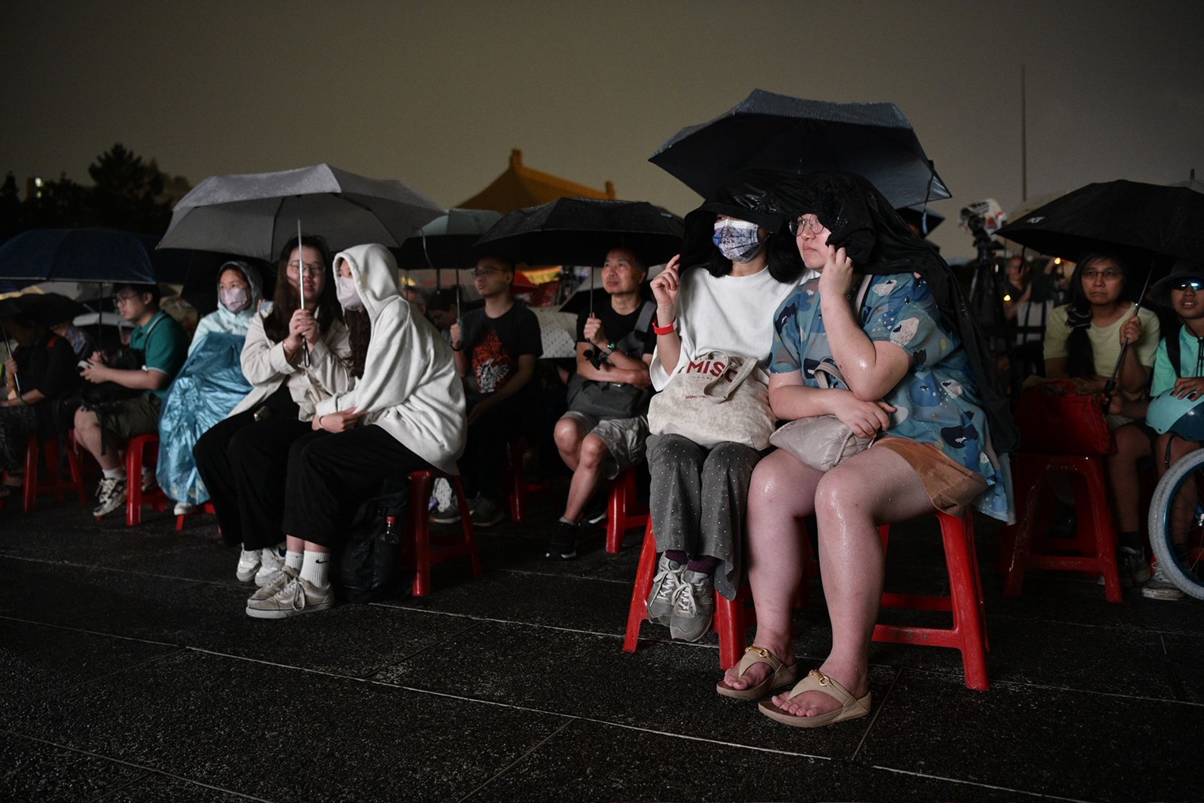 民眾不畏天空飄著雨,穿著雨衣、撐起傘在晚會致意。(鏡報李智為攝)