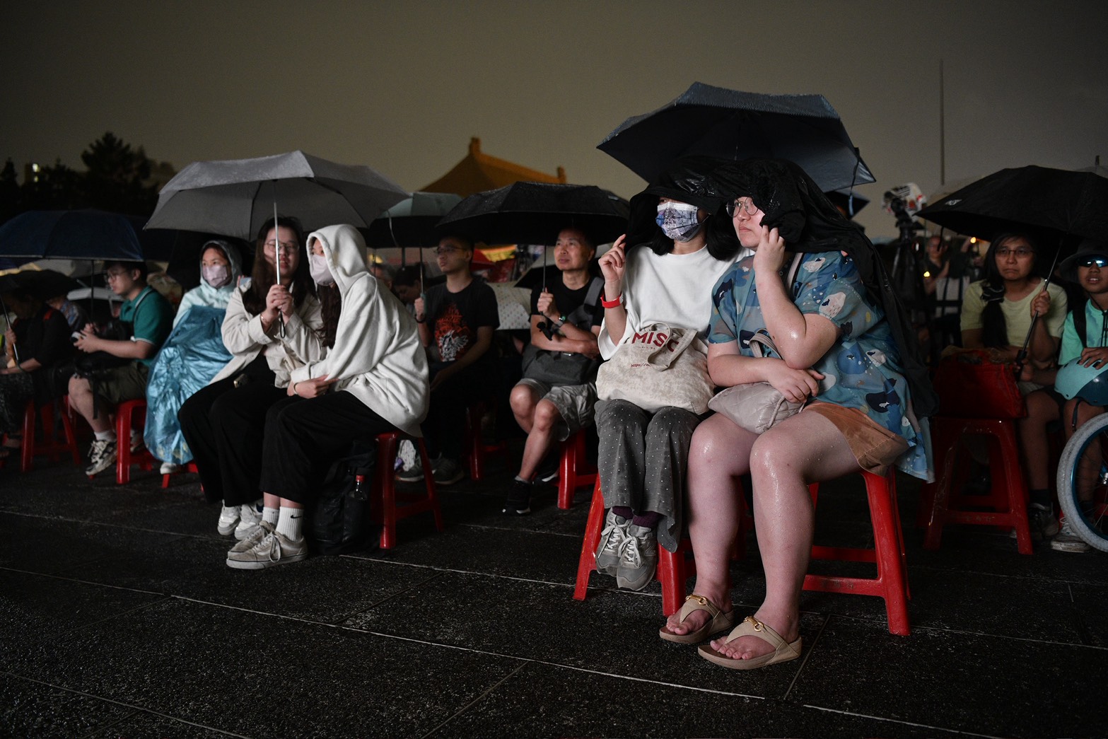 民眾不畏天空飄著雨，穿著雨衣、撐起傘在晚會致意。（鏡報李智為攝）