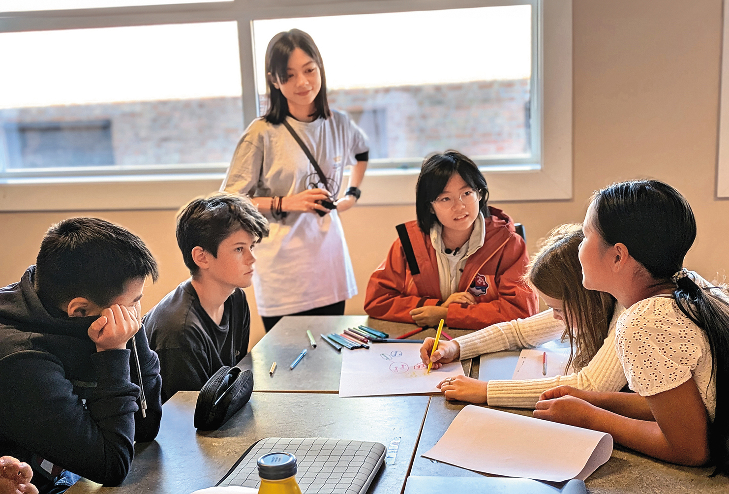 台灣小朋友與挪威學生討論氣候變遷議題,姚愛寗(站立者)專心聆聽 。(公視提供)
