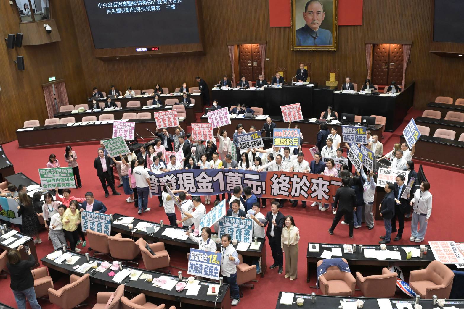 立法院今三讀通過韌性特別預算，確定將普發現金1萬元，各黨團開心拍照，羅明才又拿起1萬元在手上揮舞。（鏡報林煒凱）