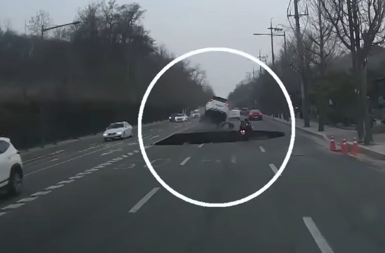前方白色轎車幸運閃過,但後方騎士閃避不及,掉入天坑。(翻攝自YouTube頻道연합뉴스TV)