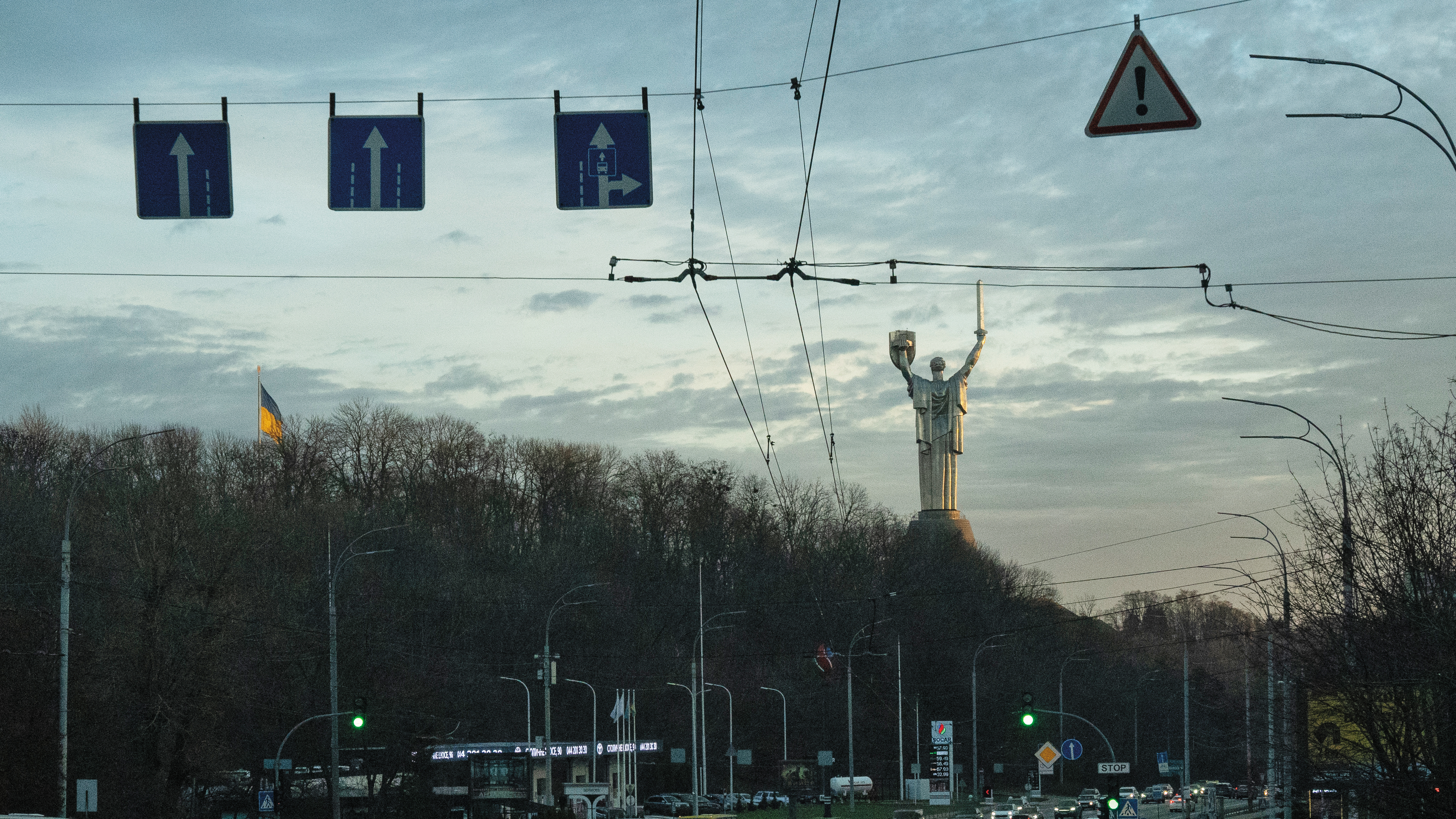 在清晨的車流中,遠處的烏克蘭母親(Mother Ukraine)紀念碑呈現極具代表性的轉變—在2023年,烏克蘭的三叉戟(Tryzub)取代了盾牌上原本的蘇聯國徽。此舉象徵烏國不斷轉變的身分和獨立狀態。
