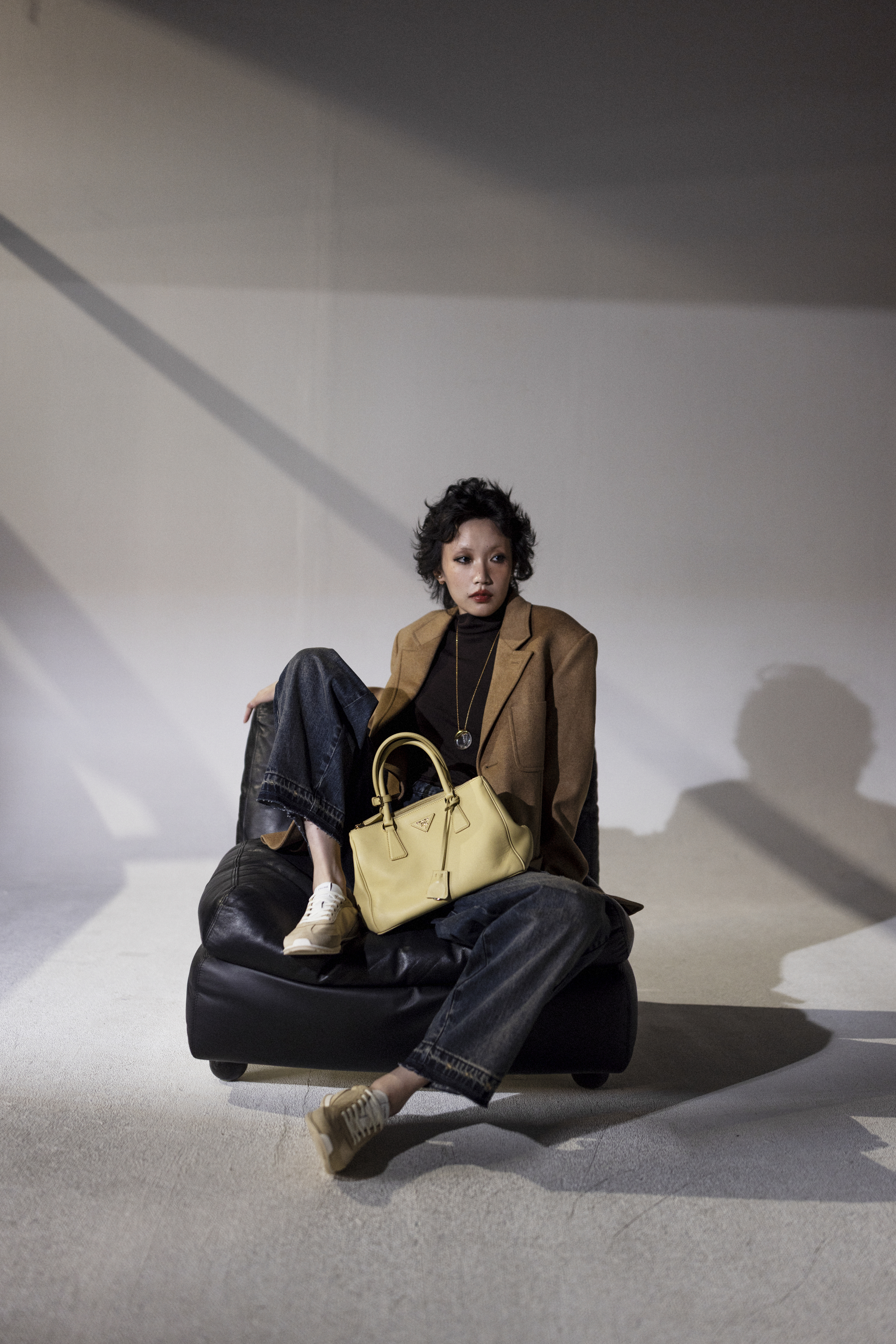 Galleria軟皮革肩背包 NT$175,000 by PRADA／西裝外套 NT$138,000 by CELINE／咖啡色高領上衣 NT$30,000 by CELINE／茶染丹寧褲 NT$16,200 by MAX&Co.／Racer運動鞋 NT$28,500 by CELINE／Tribales D-Ornemental玫瑰金色珠飾耳環 NT$19,500 by DIOR／Les Pierres項鍊 NT$28,500 by CELINE