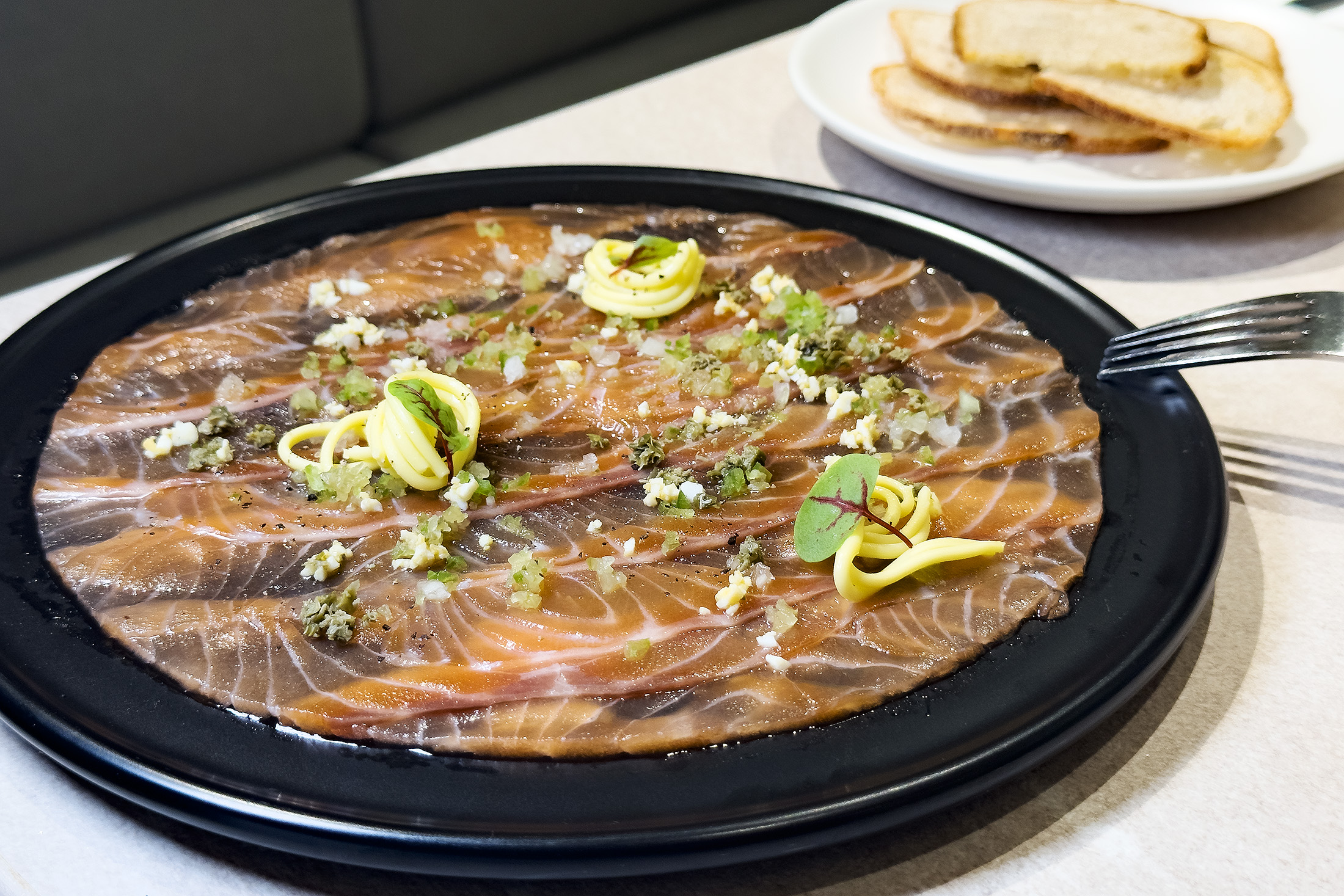 「自製鮭魚薄片」以獨特手法將生食級鮭魚醃漬後，切成晶瑩薄片，搭配多種佐料與無鹽奶油，吃的是食材的純粹鮮甜。（420元／份）